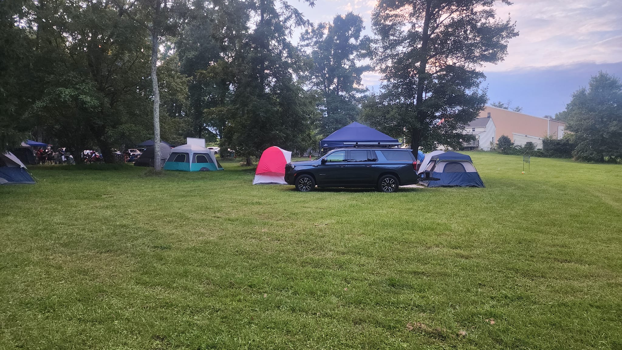 Tents and a large SUV with rooftop canopy set up across the open lawn at dusk — Campout 2023