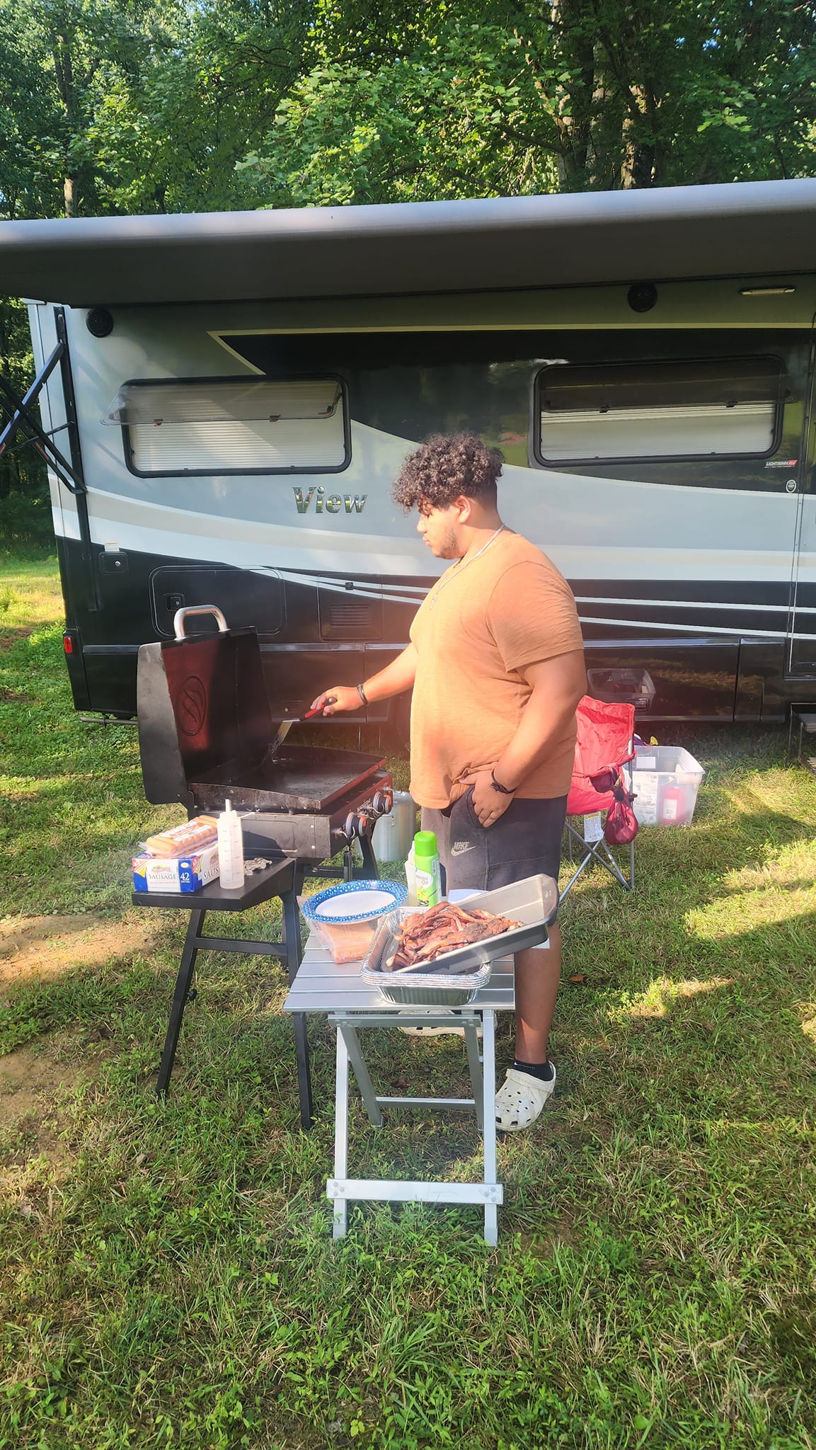 Grilling ribs in front of the RV in an orange shirt — Campout 2023