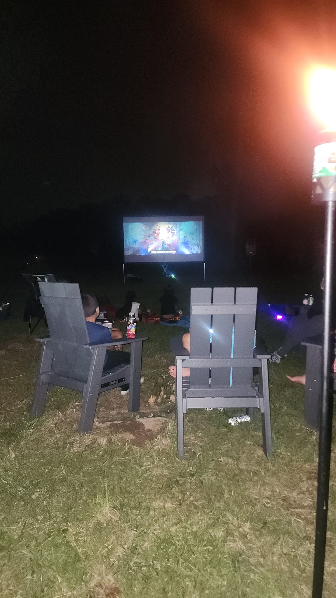 Watching the outdoor movie screen from Adirondack chairs at night — Campout 2023