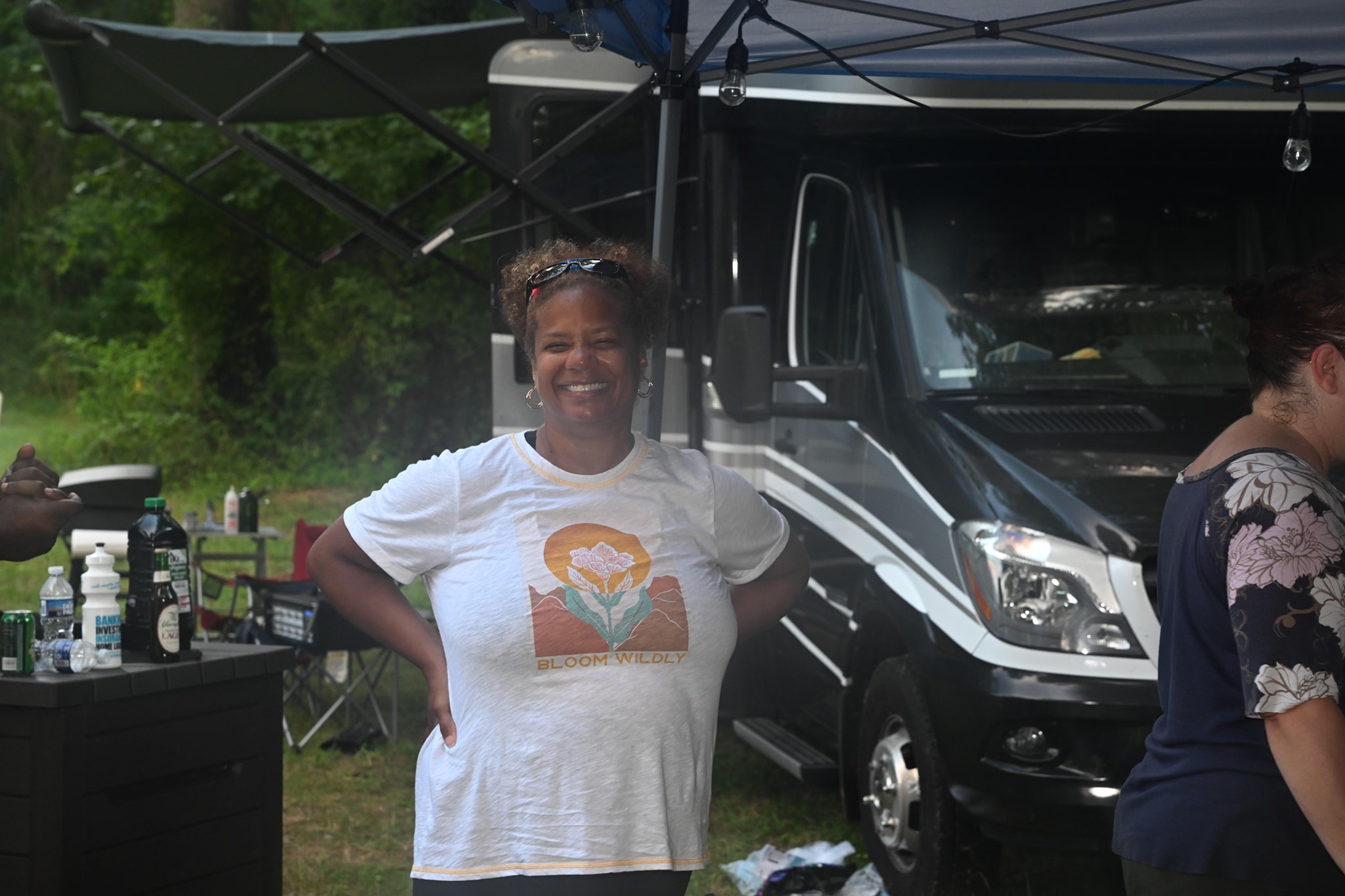 Smiling in front of the RV in a graphic tee with hands on hips — Campout 2023