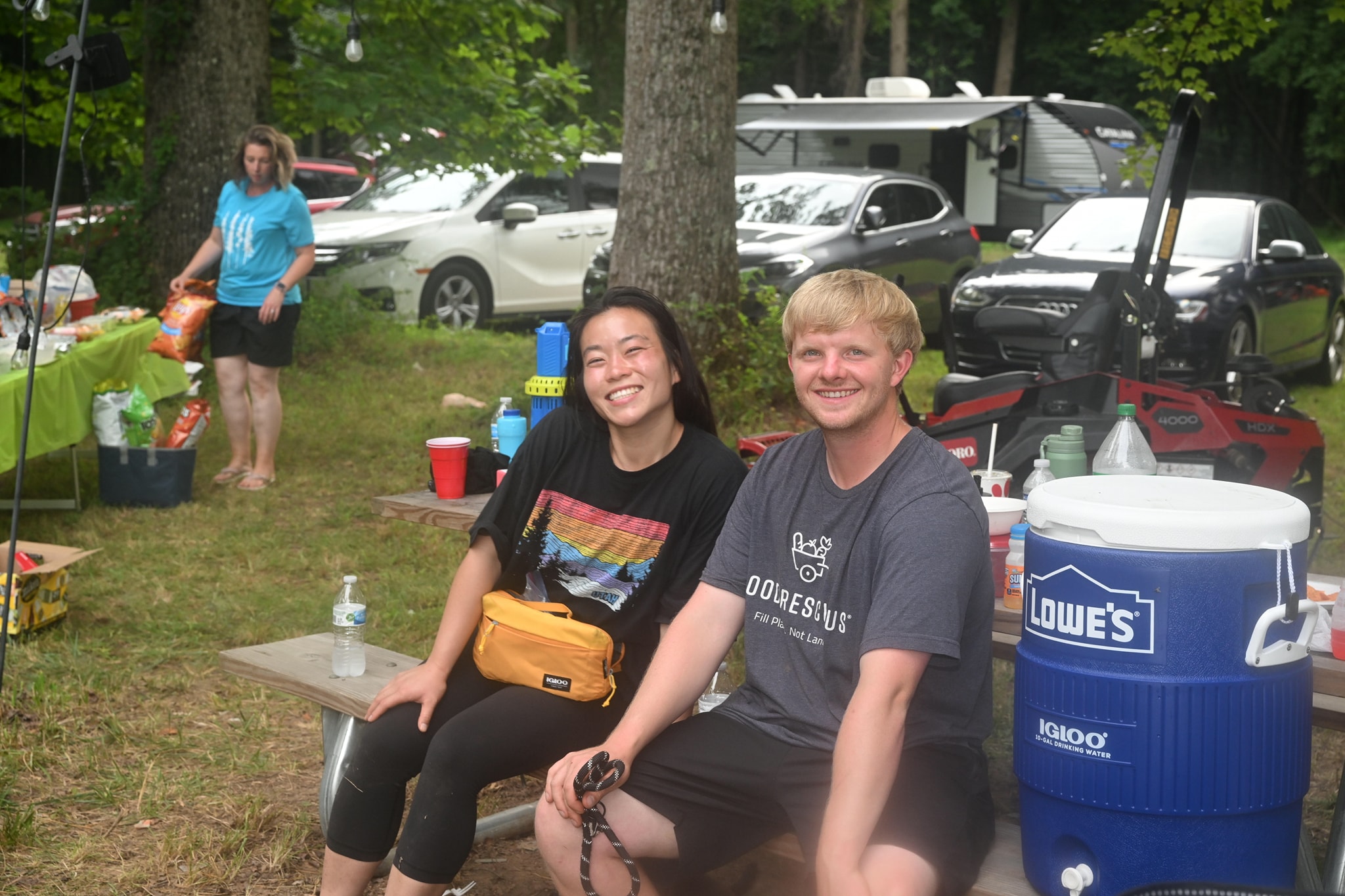 A couple smiling together on a bench in the wooded campsite — Campout 2023