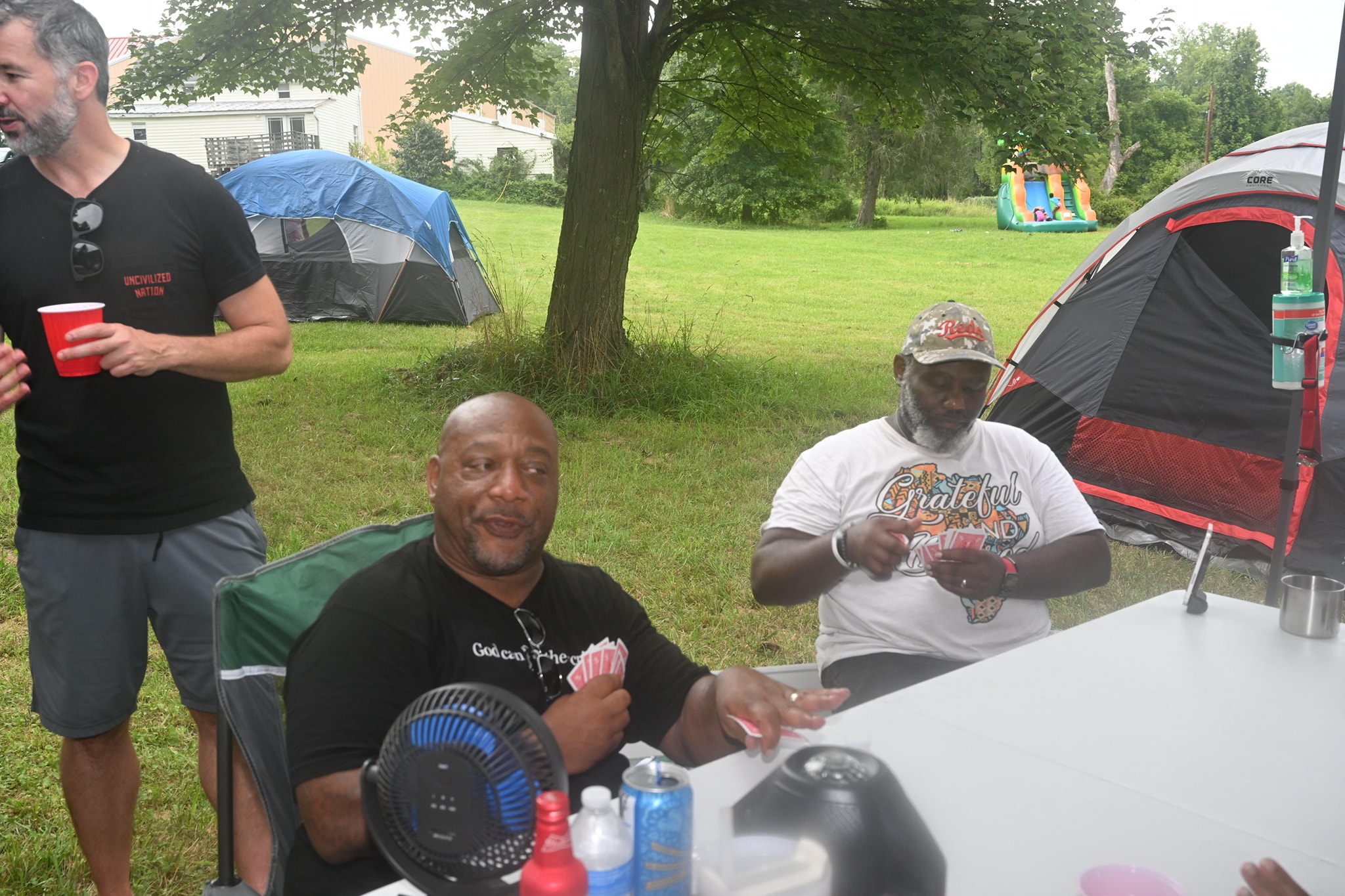Guests playing cards at a table with tents and the bounce house visible in the background — Campout 2023