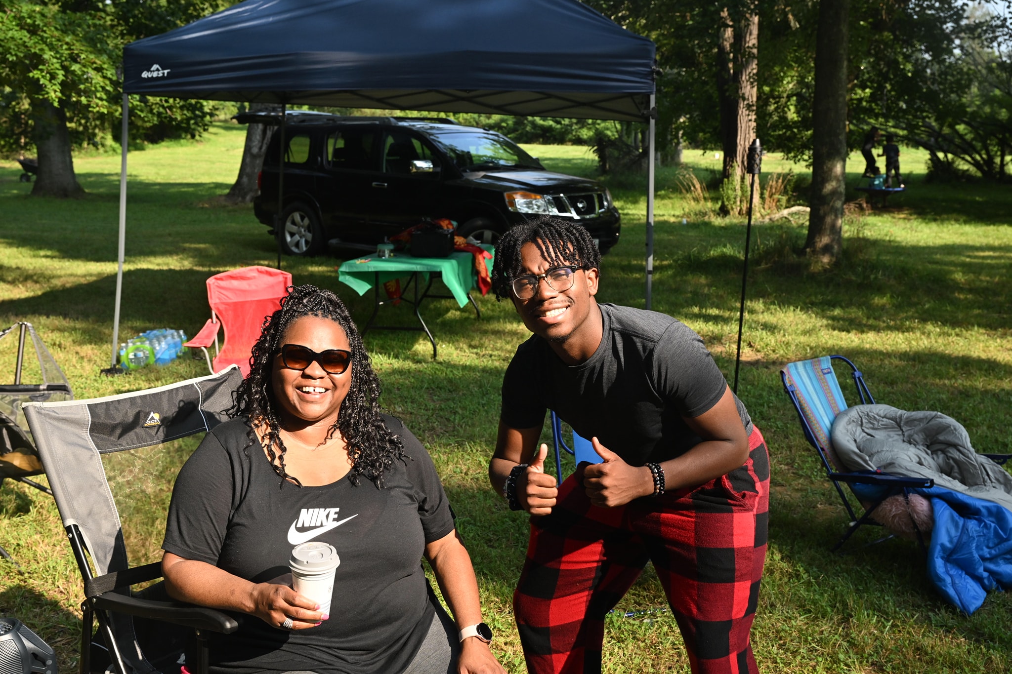 A mom and son smiling together under the canopy tent at golden hour — Campout 2023