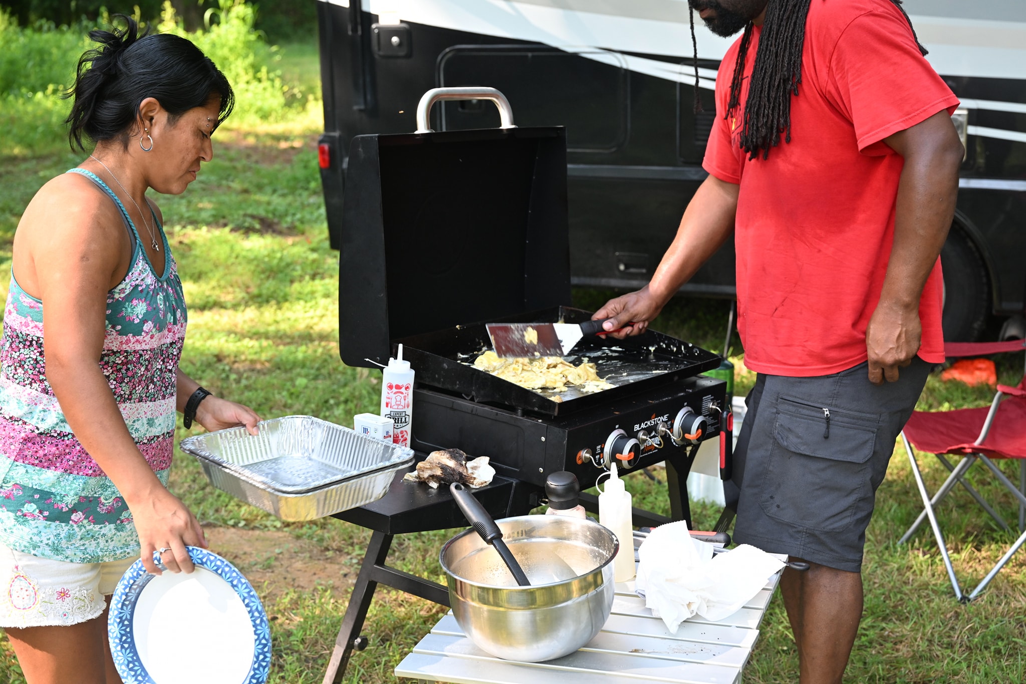 Two people cooking on a flat-top griddle beside the RV — Campout 2023