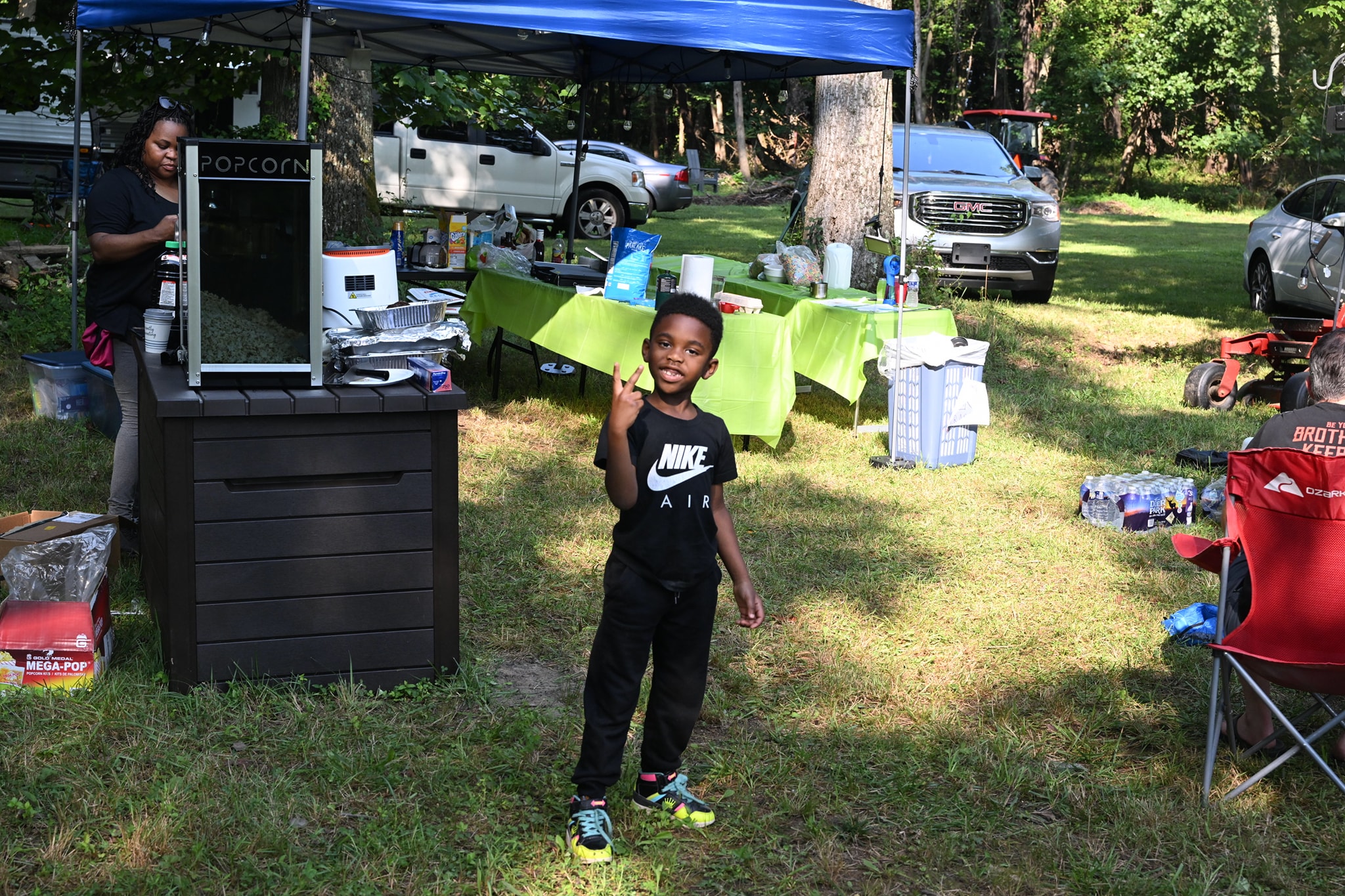 A little boy in a Nike Air shirt pointing confidently near the popcorn machine — Campout 2023