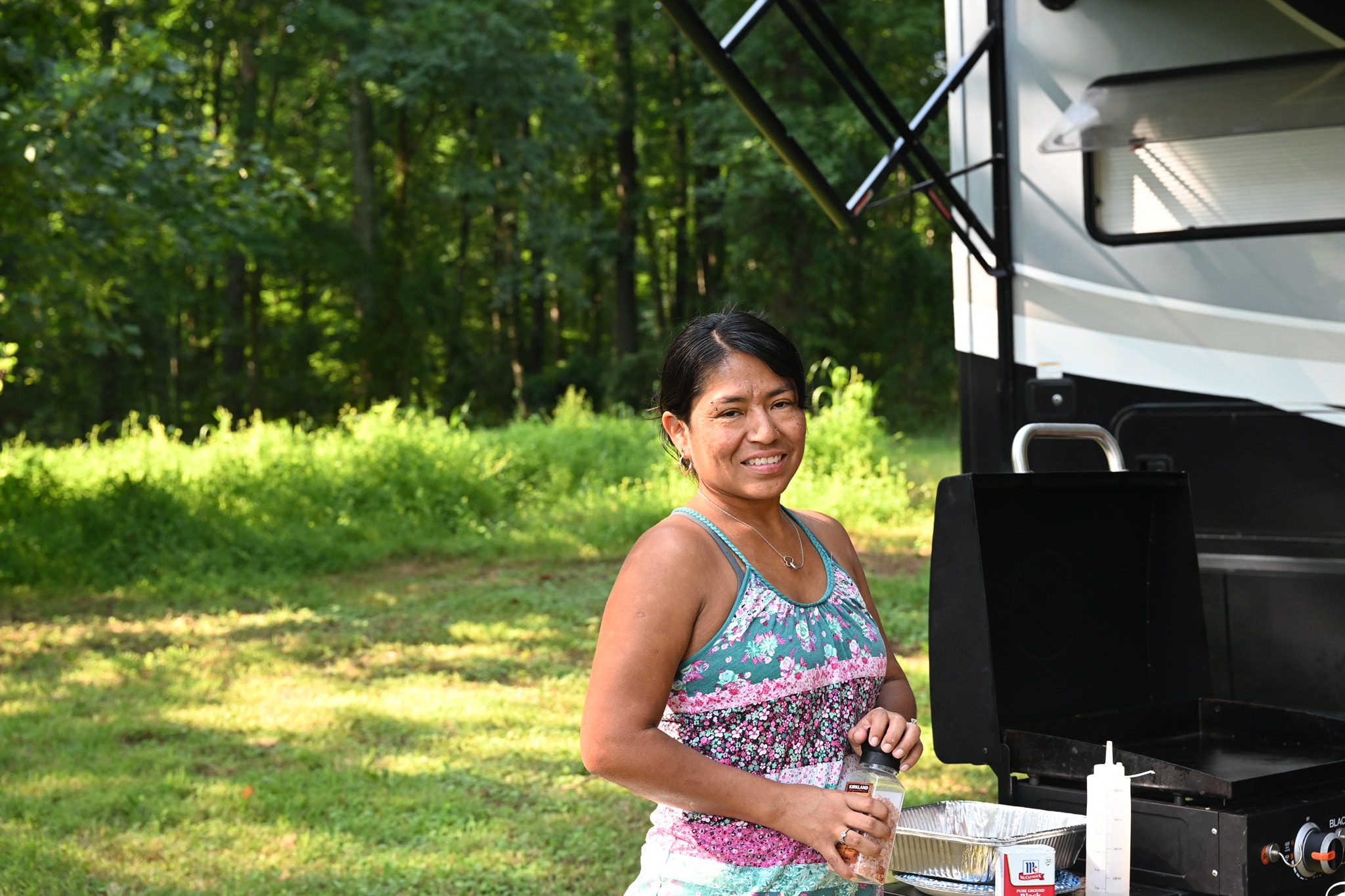 Smiling beside the griddle grill next to the RV on a sunny afternoon — Campout 2023