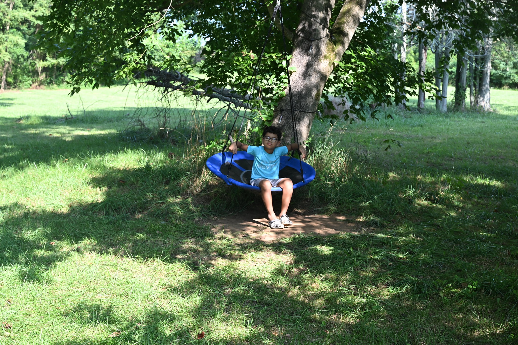 A boy relaxing in a large saucer tree swing in the shade — Campout 2023