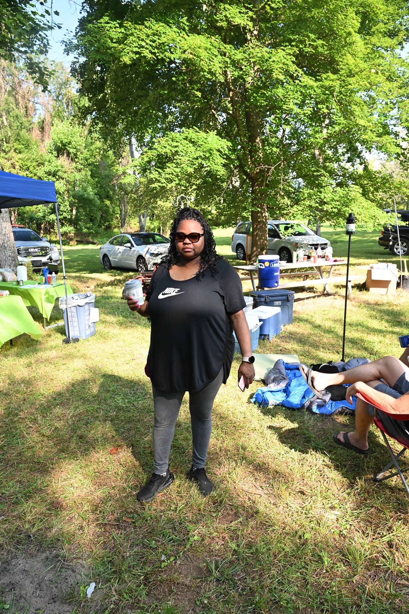 Standing on the lawn in sunglasses with a drink, canopy tents and food tables in the background — Campout 2023
