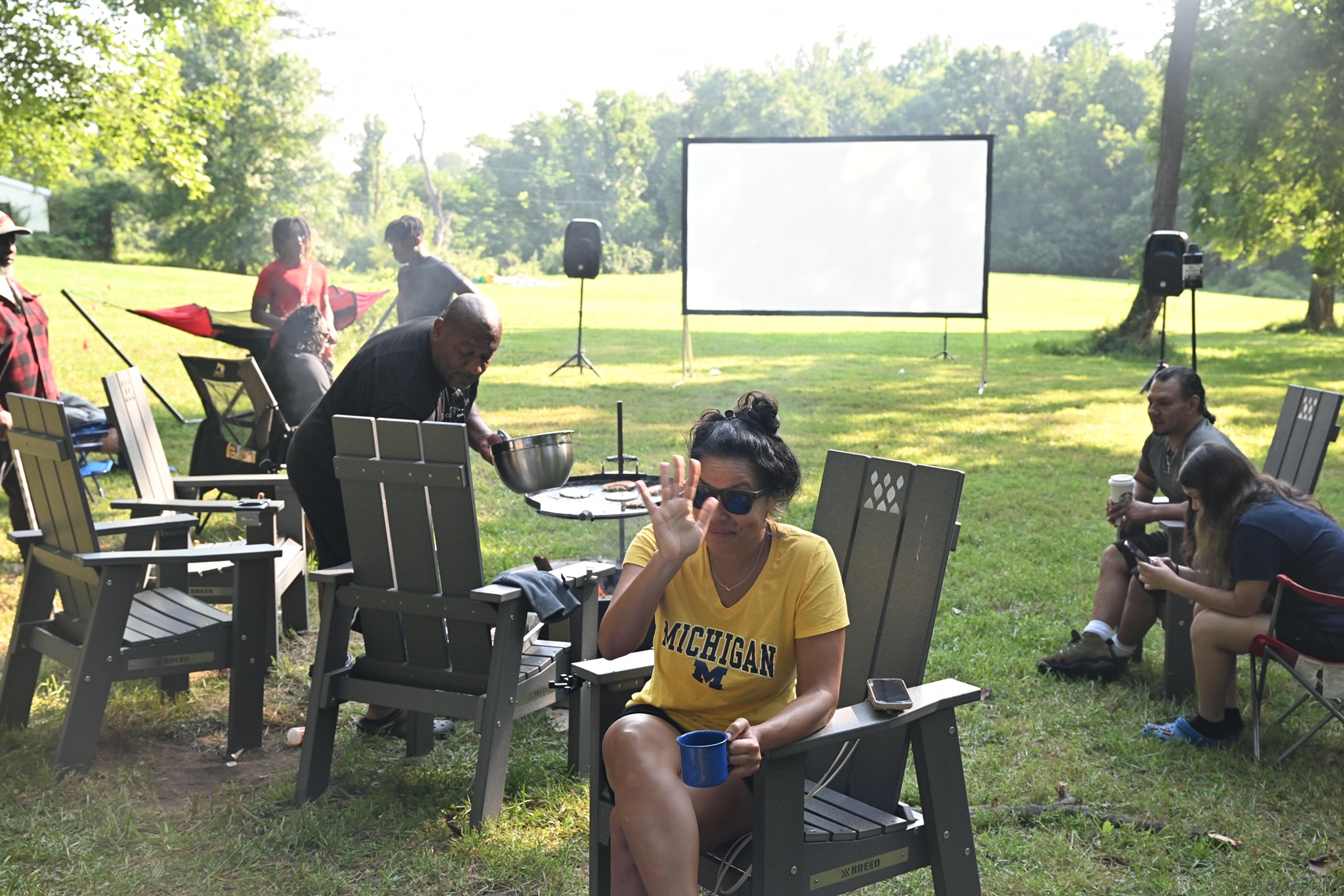 Relaxing in an Adirondack chair in a Michigan shirt with the movie screen set up behind — Campout 2023