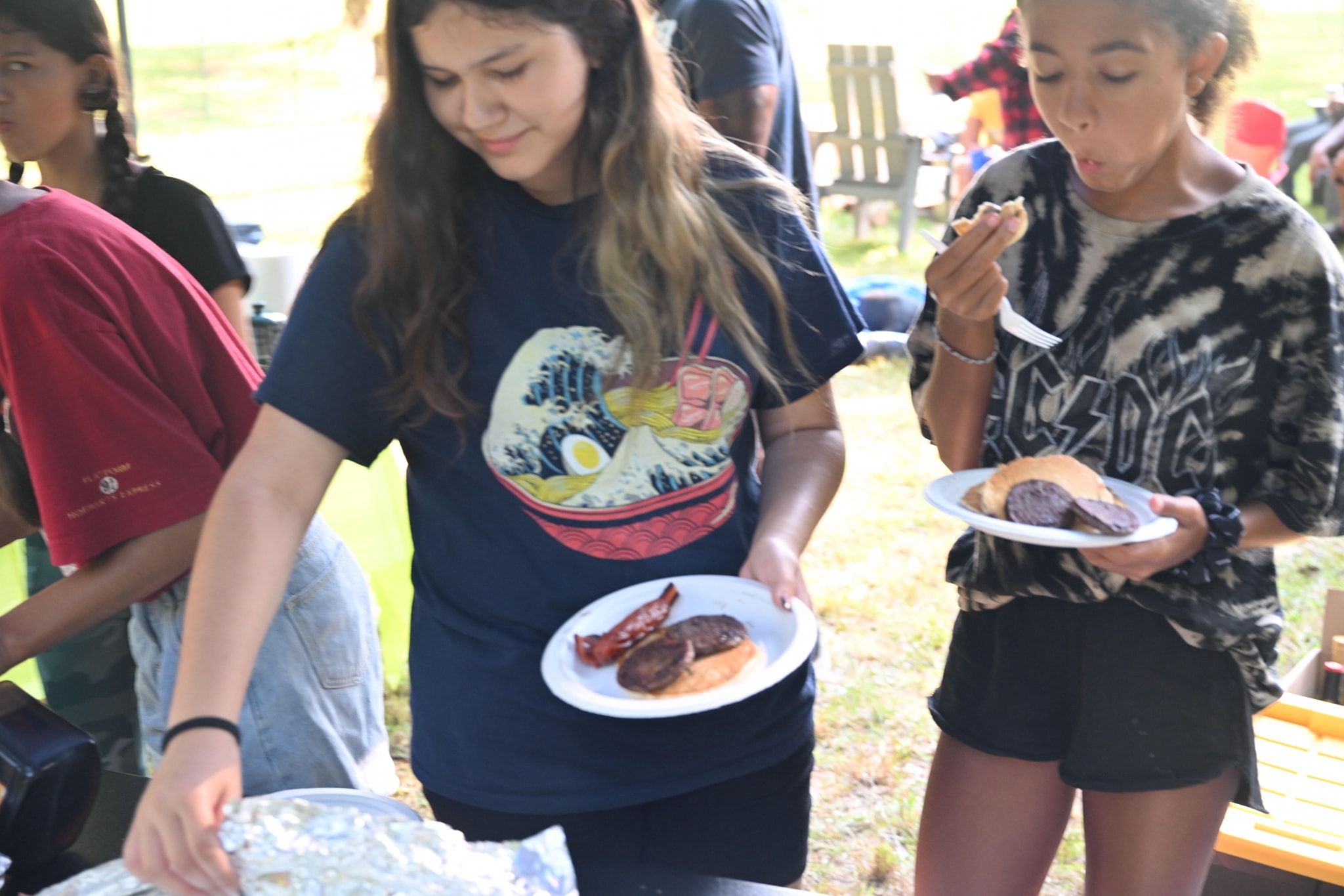 Two teens loading their plates with ribs, bacon, and sides at the food table — Campout 2023