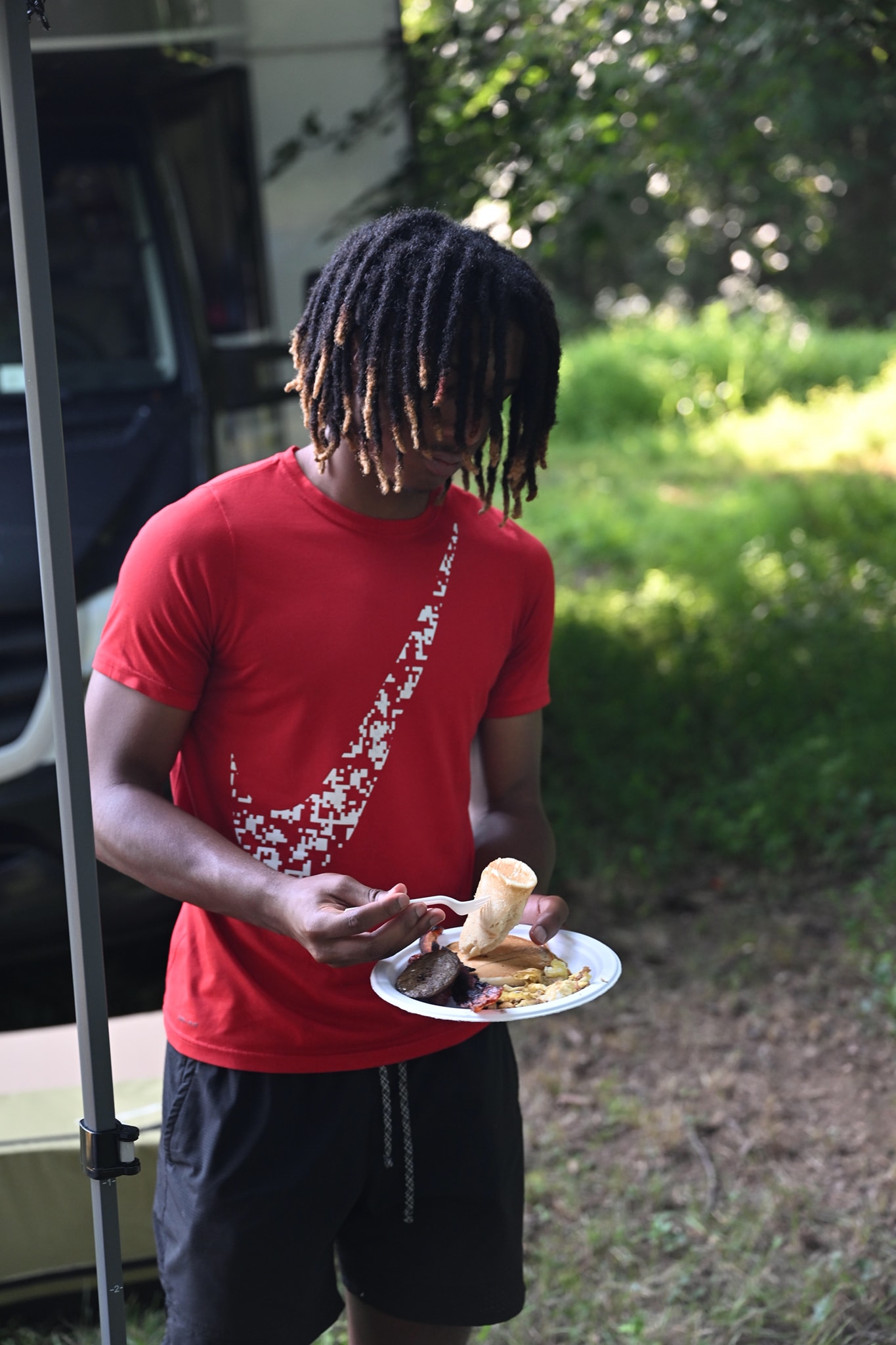 A young man in a red Nike shirt loading up a plate of food beside the RV — Campout 2023