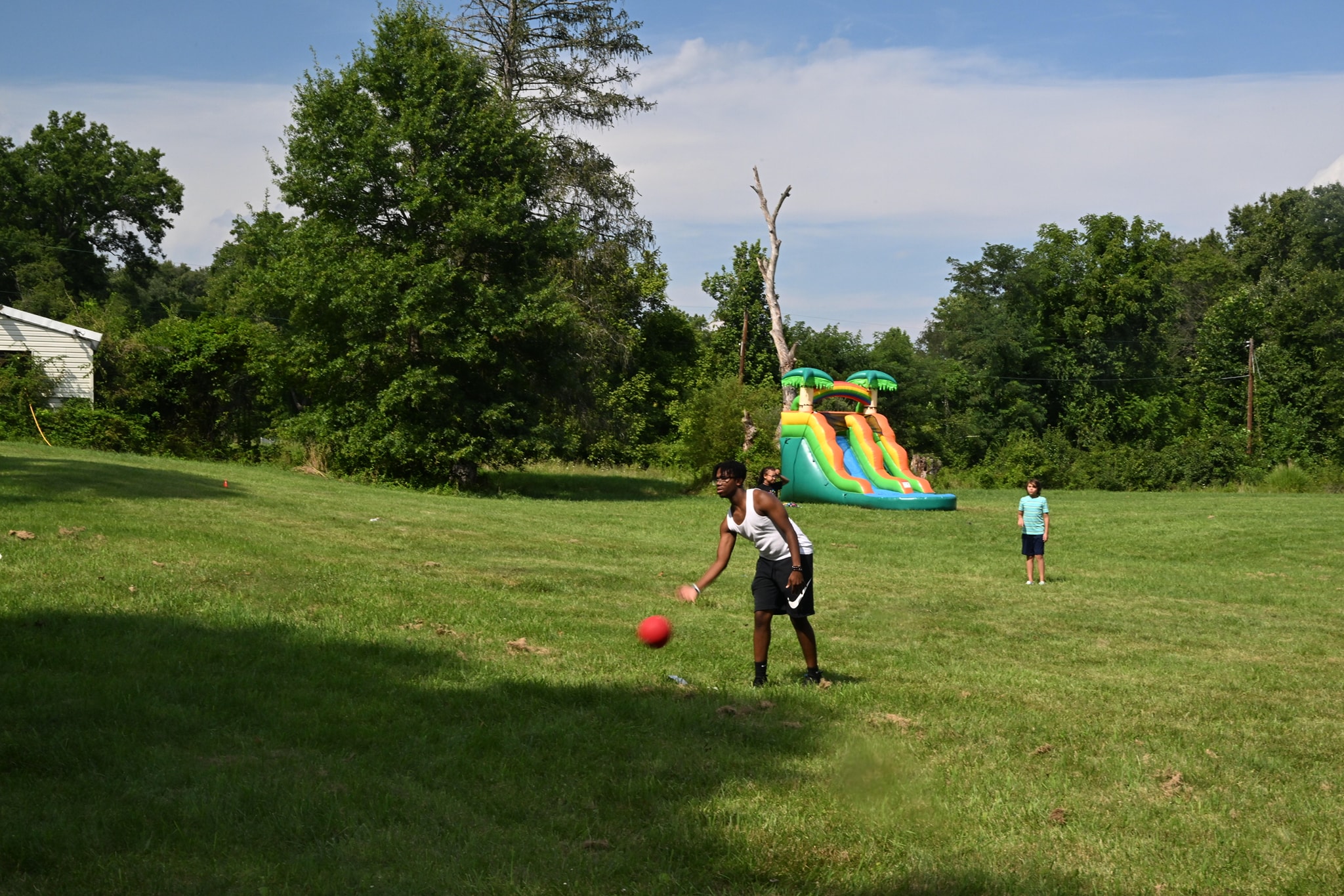 A kid throwing a red ball on the open lawn with the bounce house slide in the background — Campout 2023
