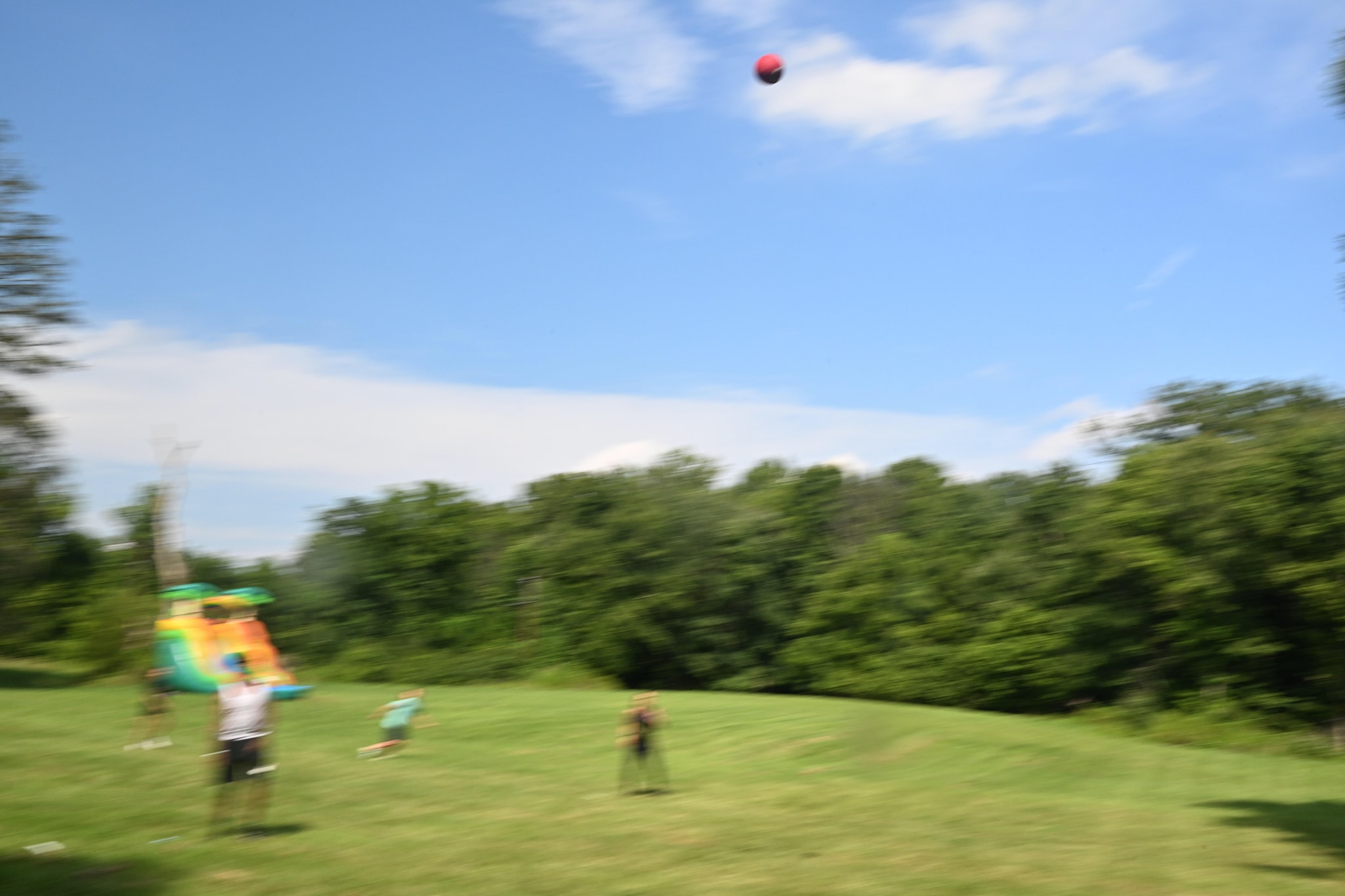 Kids playing in the open lawn with a red ball soaring in the air, bounce house behind — Campout 2023
