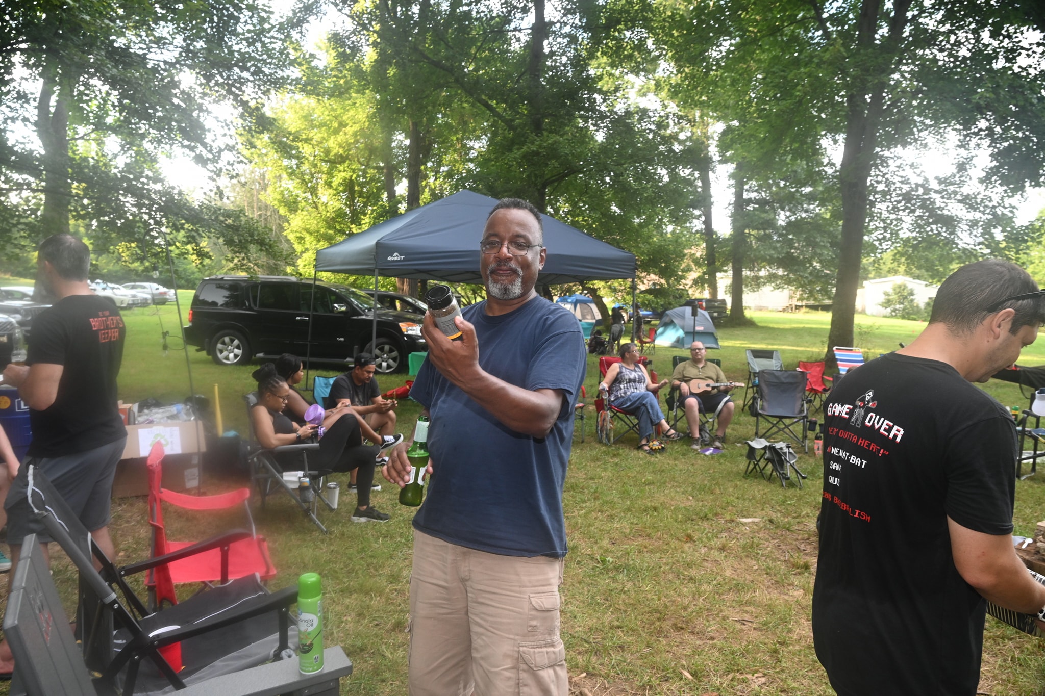 A man showing off a small bird he caught with the full campsite of guests behind him — Campout 2023