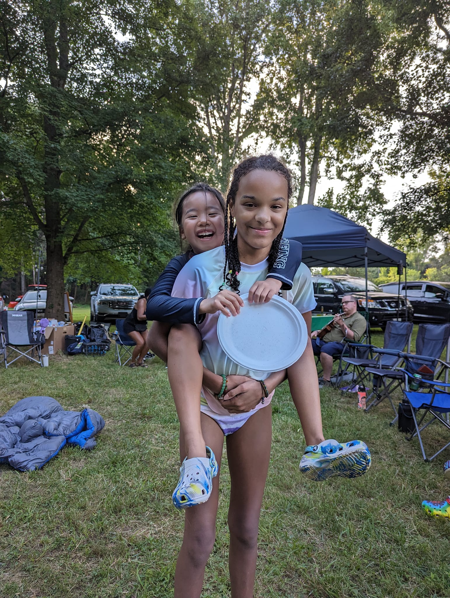 Two girls goofing around after swimming, one on the other's back holding a plate — Campout 2023