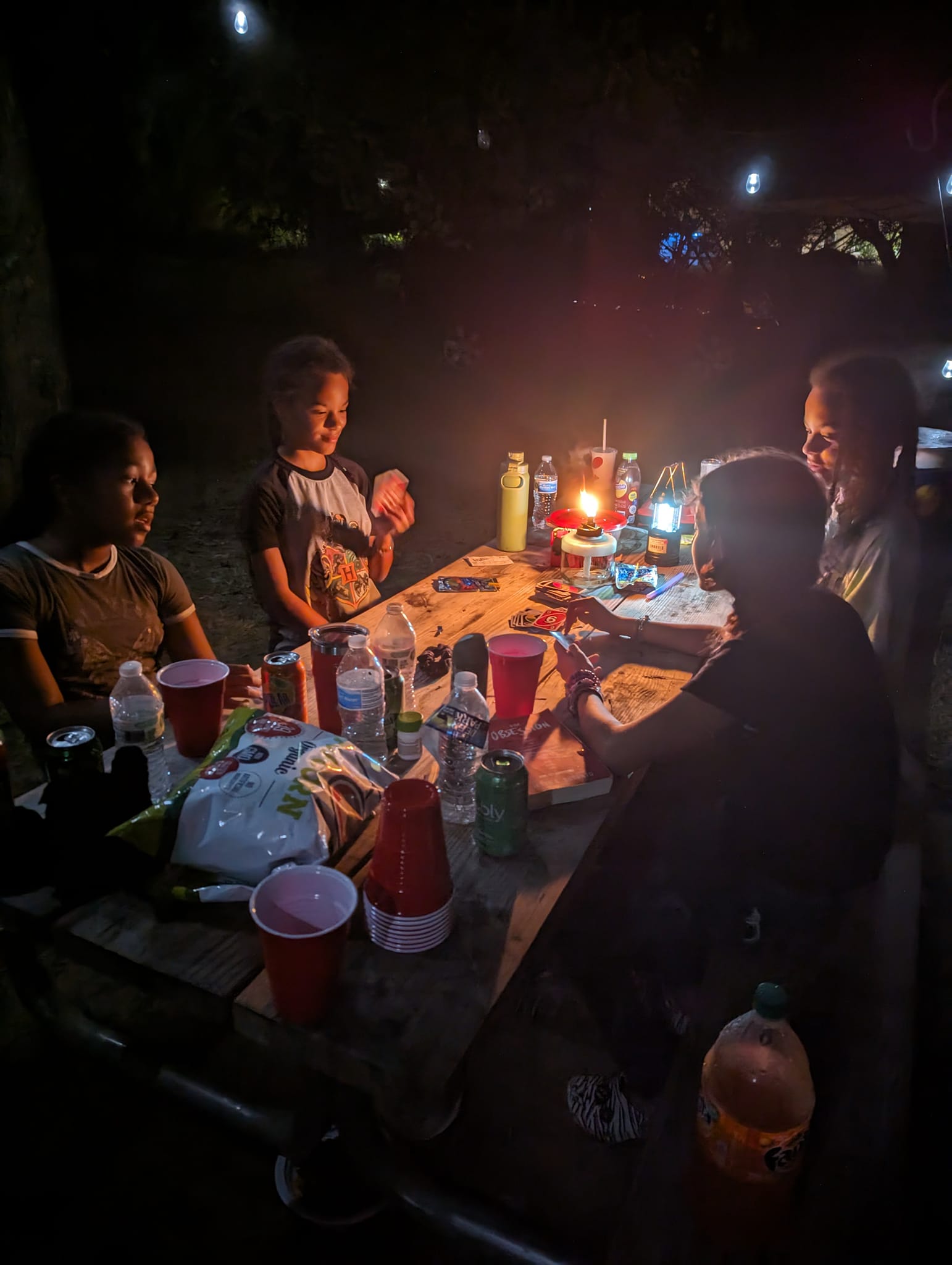 Guests playing cards at the picnic table late at night by lantern light — Campout 2023