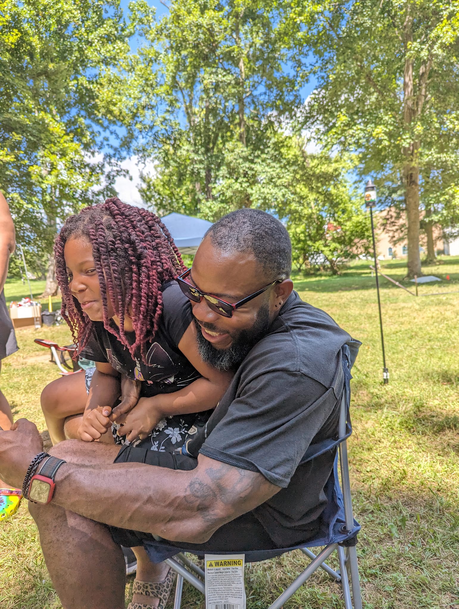 A dad and daughter sharing a moment in a camp chair in the afternoon shade — Campout 2023