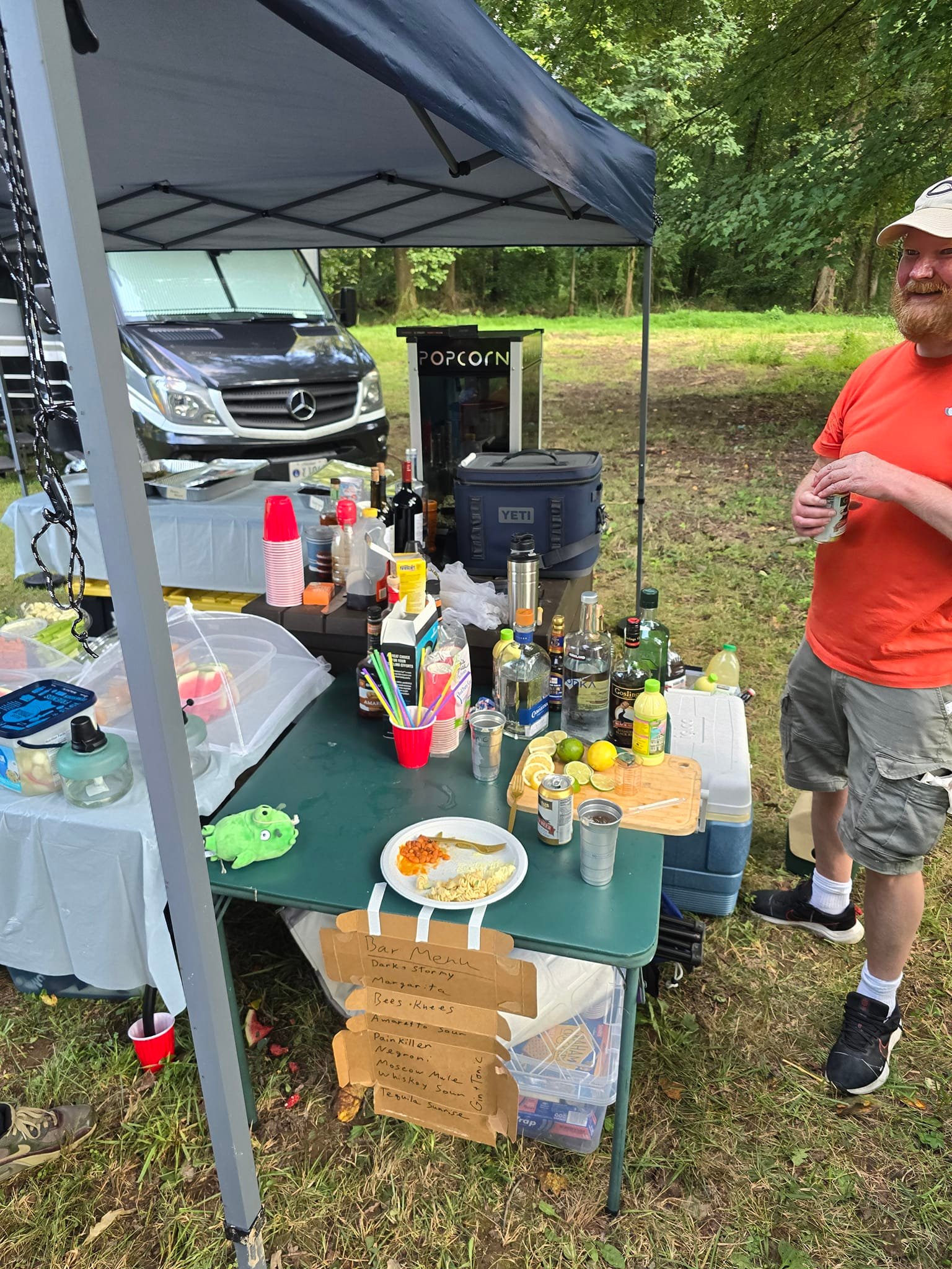Bar station setup with liquor bottles, handwritten menu, and the popcorn machine behind — Campout 2024