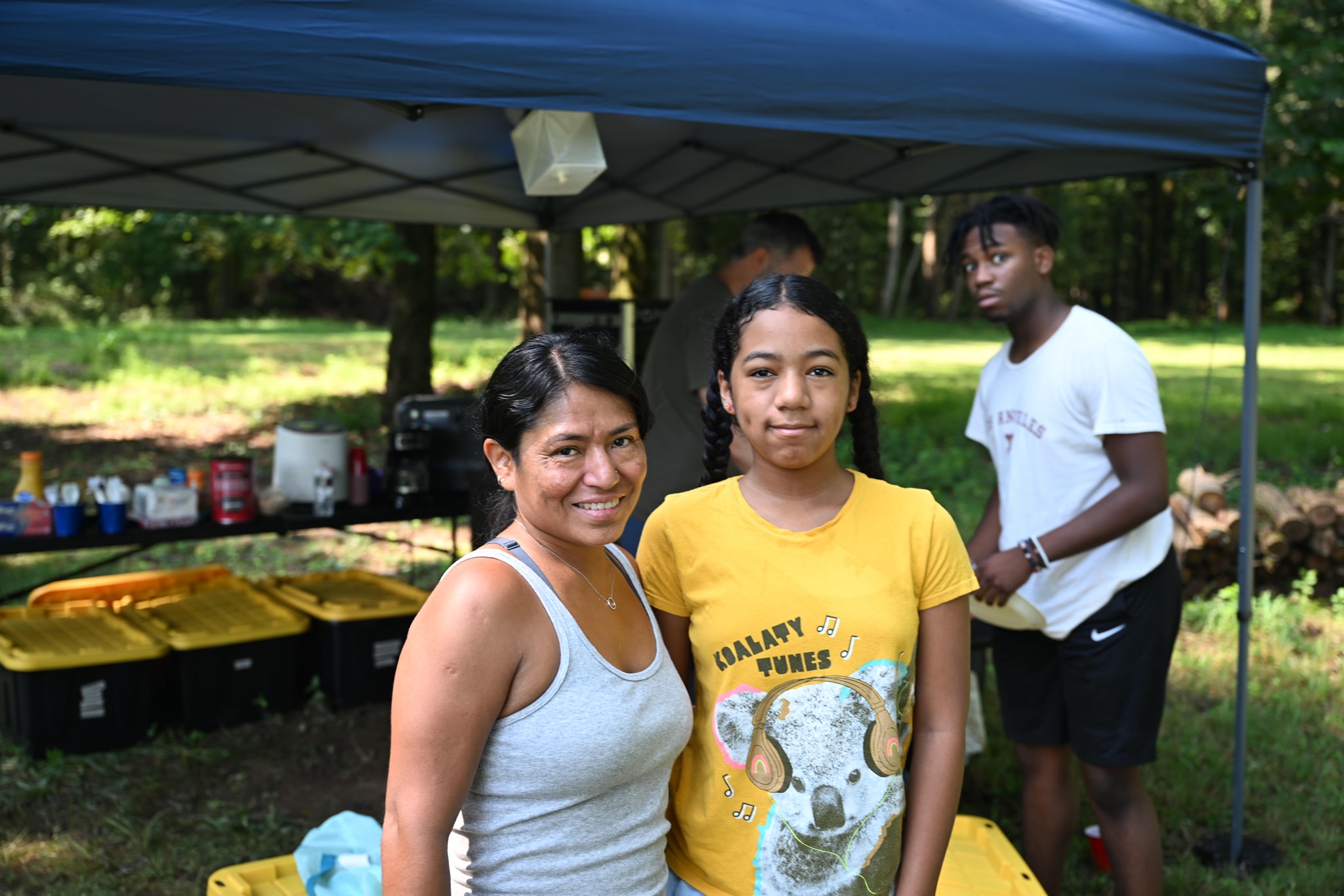 Smiling together under the food canopy with the wooded yard behind — Campout 2024