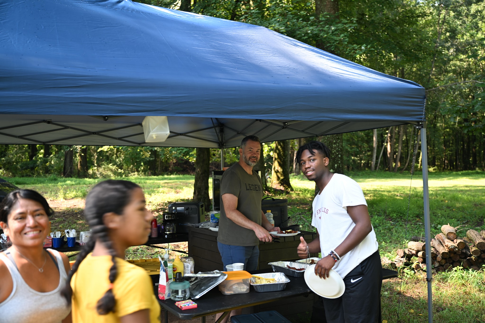Guests filling their plates at the food canopy in the wooded yard — Campout 2024