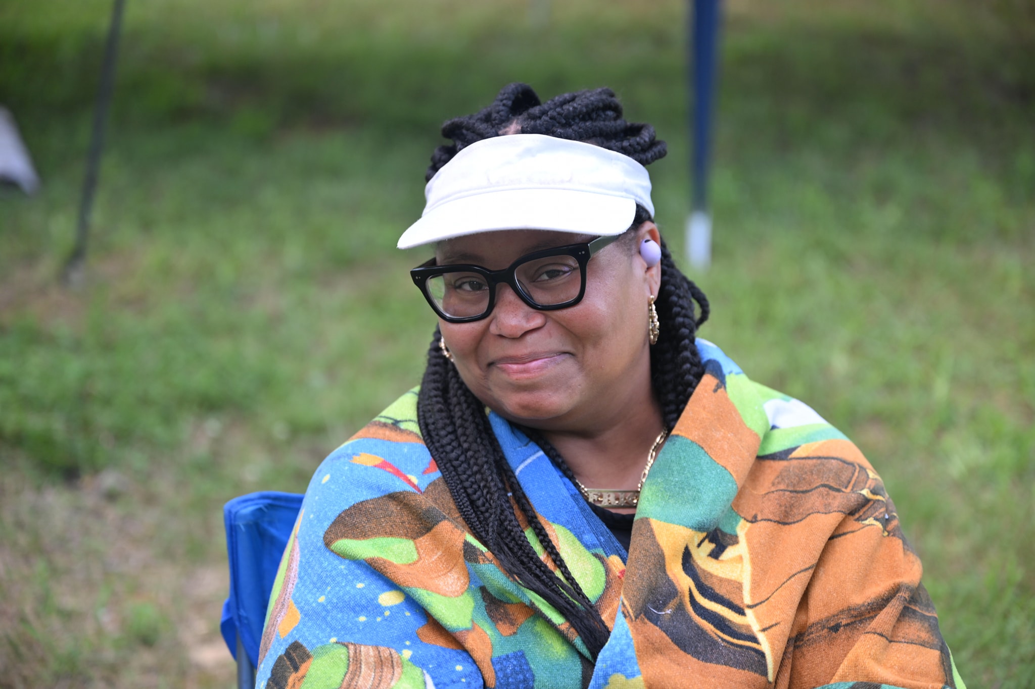 Smiling in a white visor wrapped in a colorful blanket on the lawn — Campout 2024