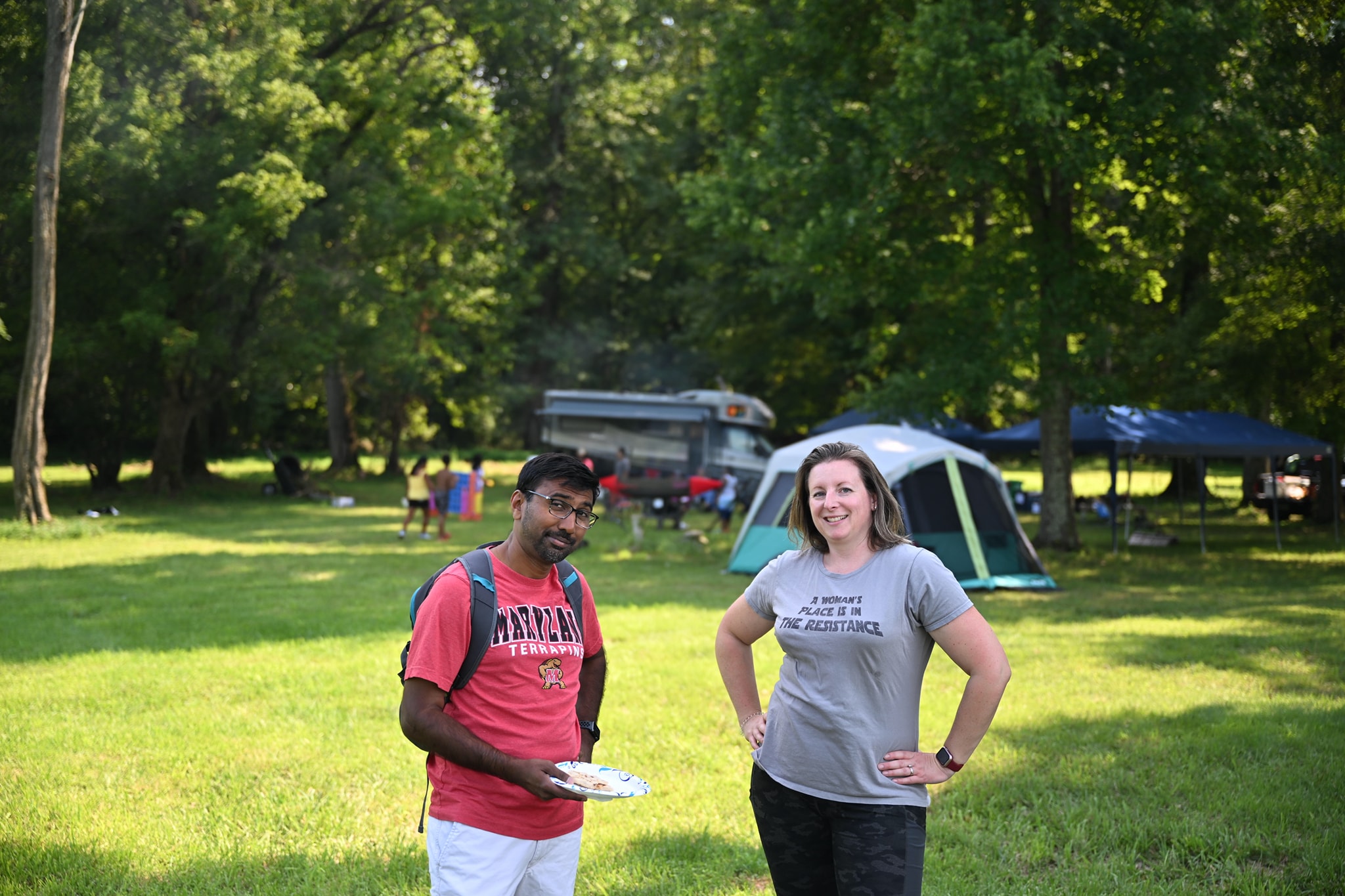 Guests smiling on the open lawn with tents and the RV in the background — Campout 2024