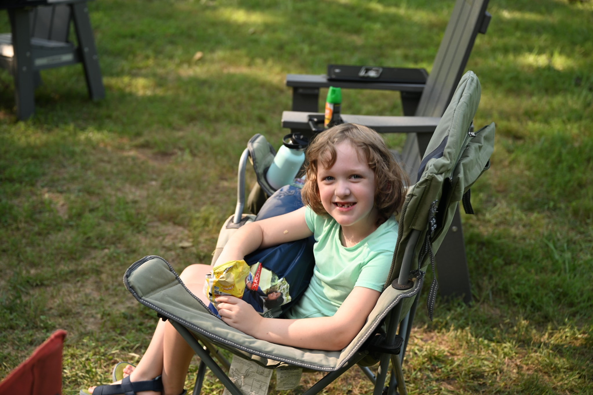 A young girl smiling in a camp chair with a snack in her lap — Campout 2024