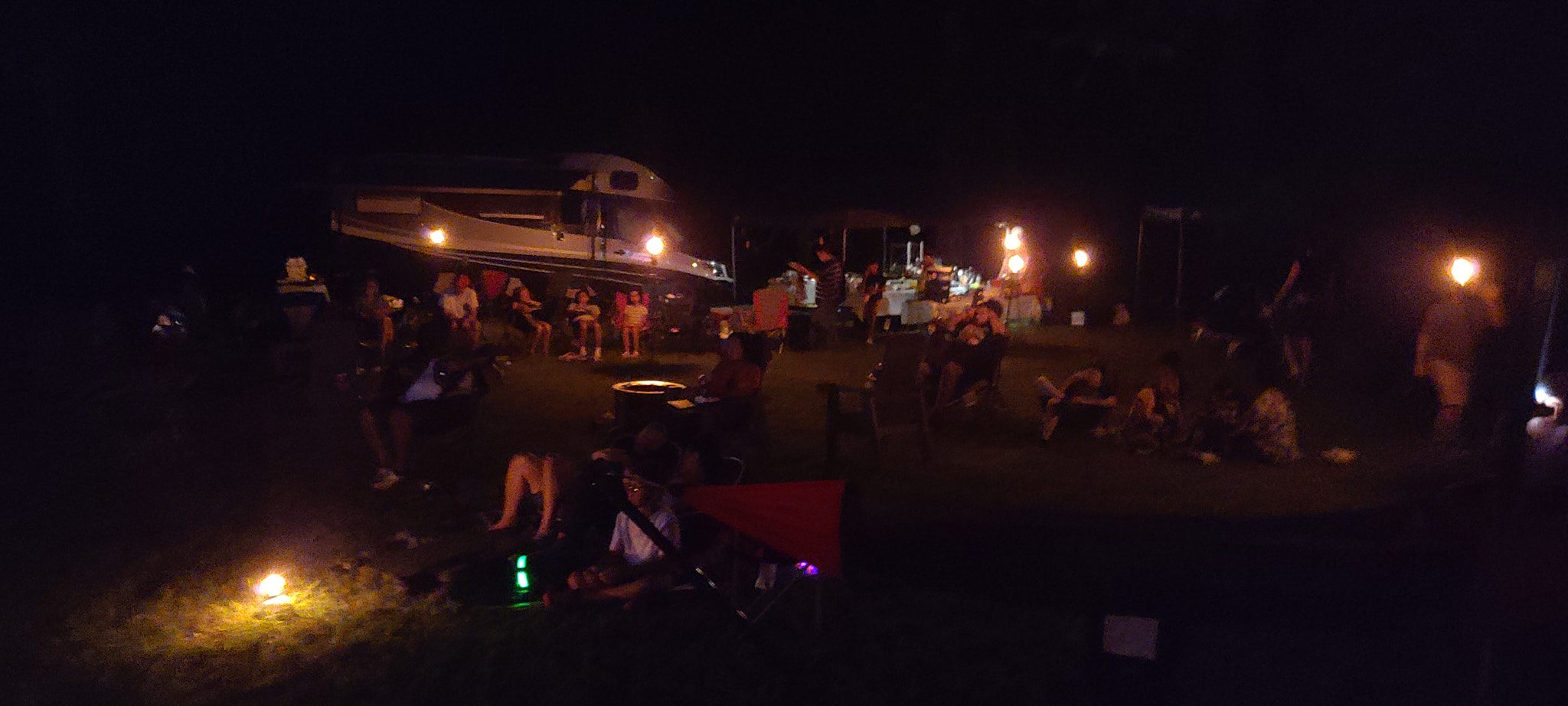 Nighttime panorama of the campout with torches and the fire pit glowing — Campout 2024