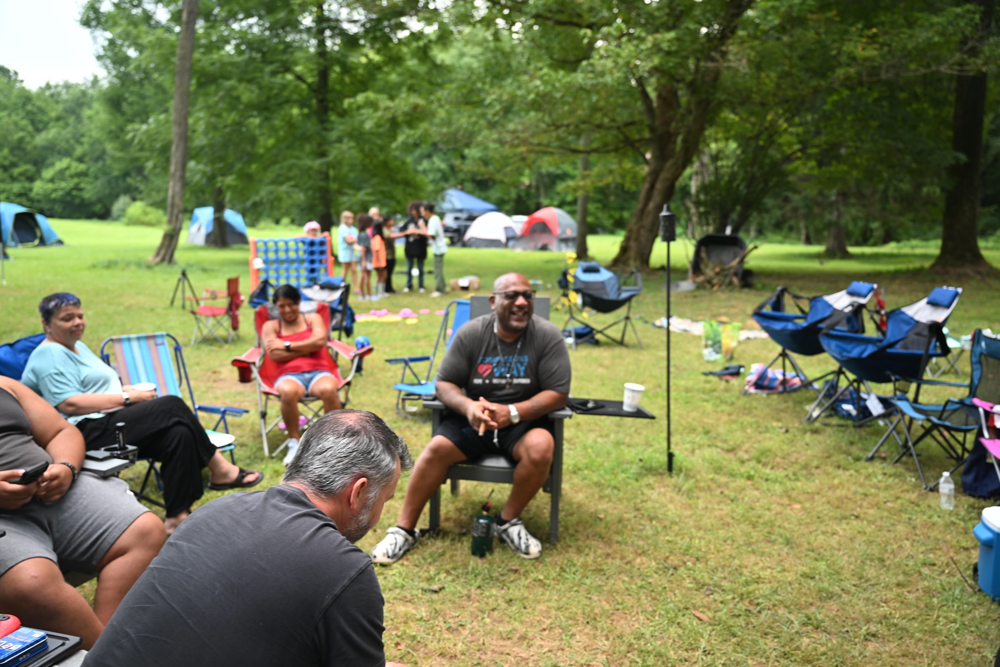 Guests relaxing and laughing in camp chairs spread across the open lawn — Campout 2024