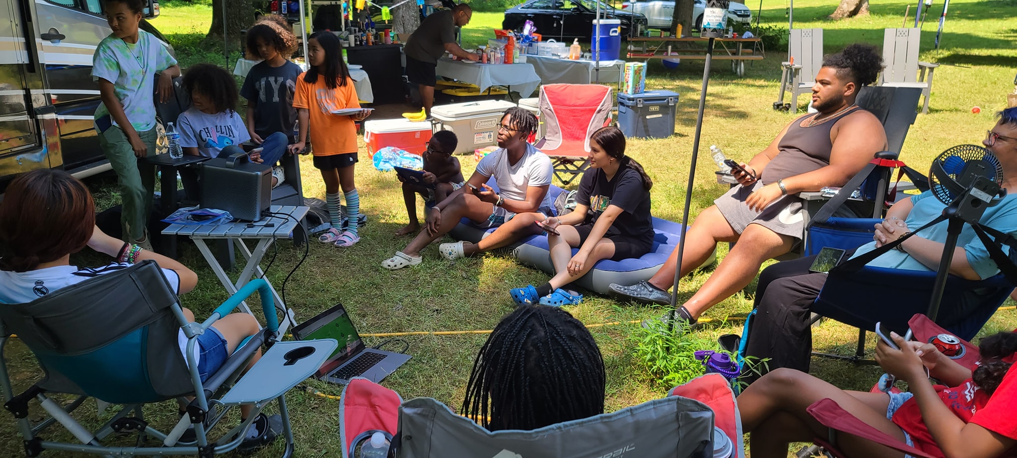 Guests sitting in a relaxed circle on the grass near the RV — Campout 2024
