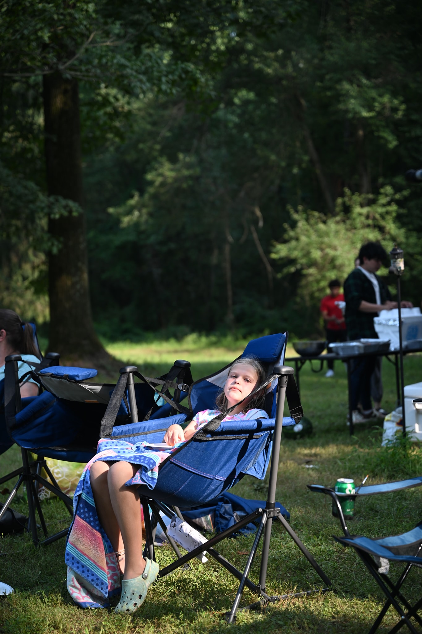 A kid resting with eyes closed in a camp chair in the afternoon shade — Campout 2024