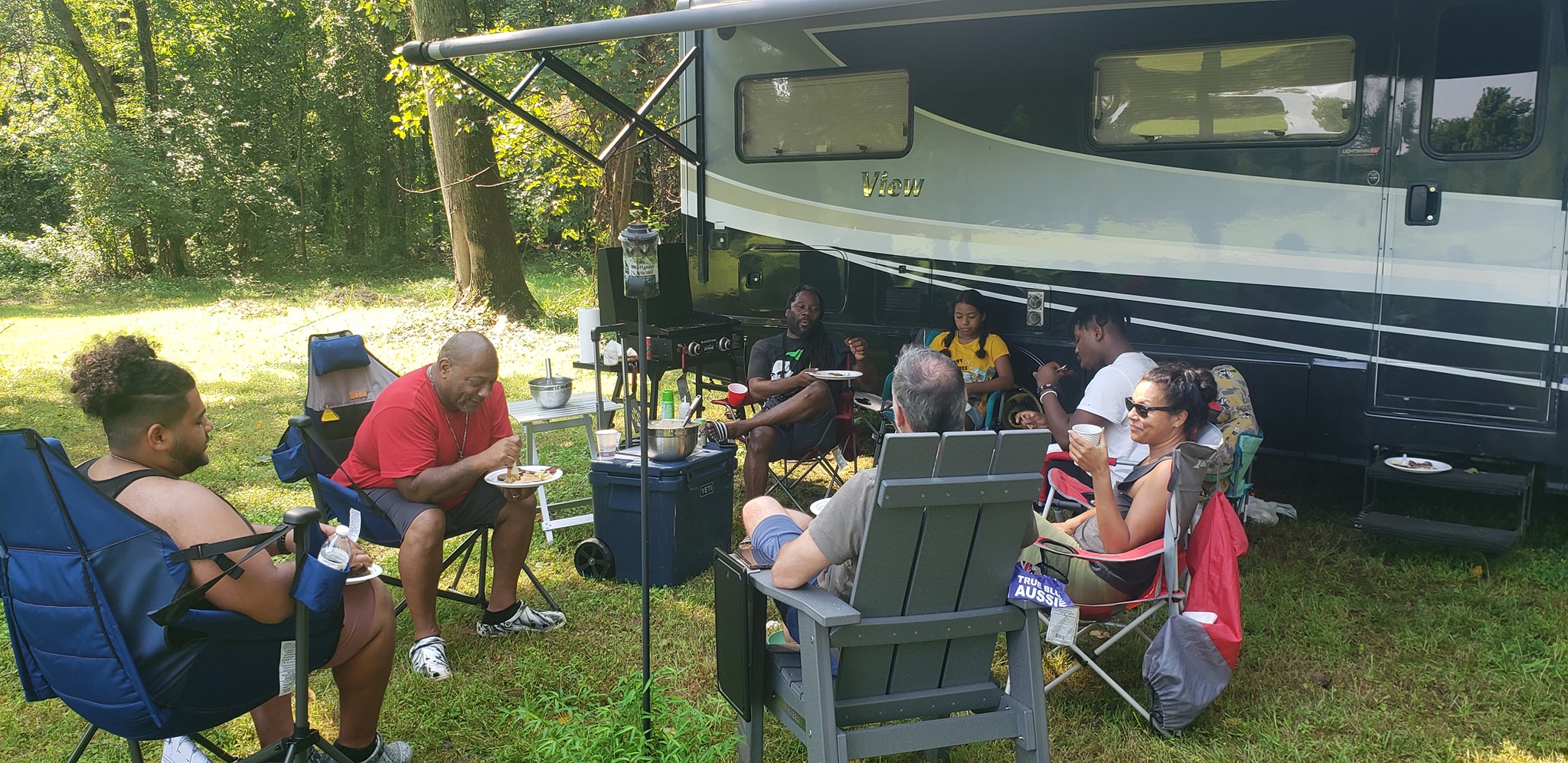 Guests eating and hanging out in camp chairs beside the RV — Campout 2024