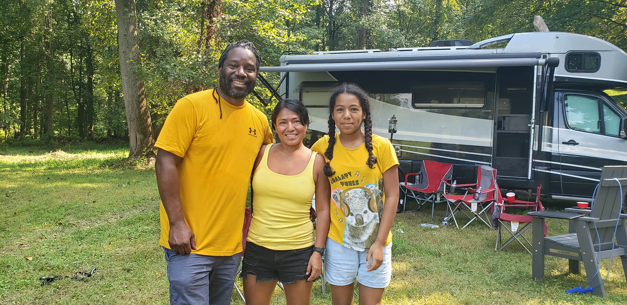 A family in matching yellow shirts smiling in front of the RV — Campout 2024