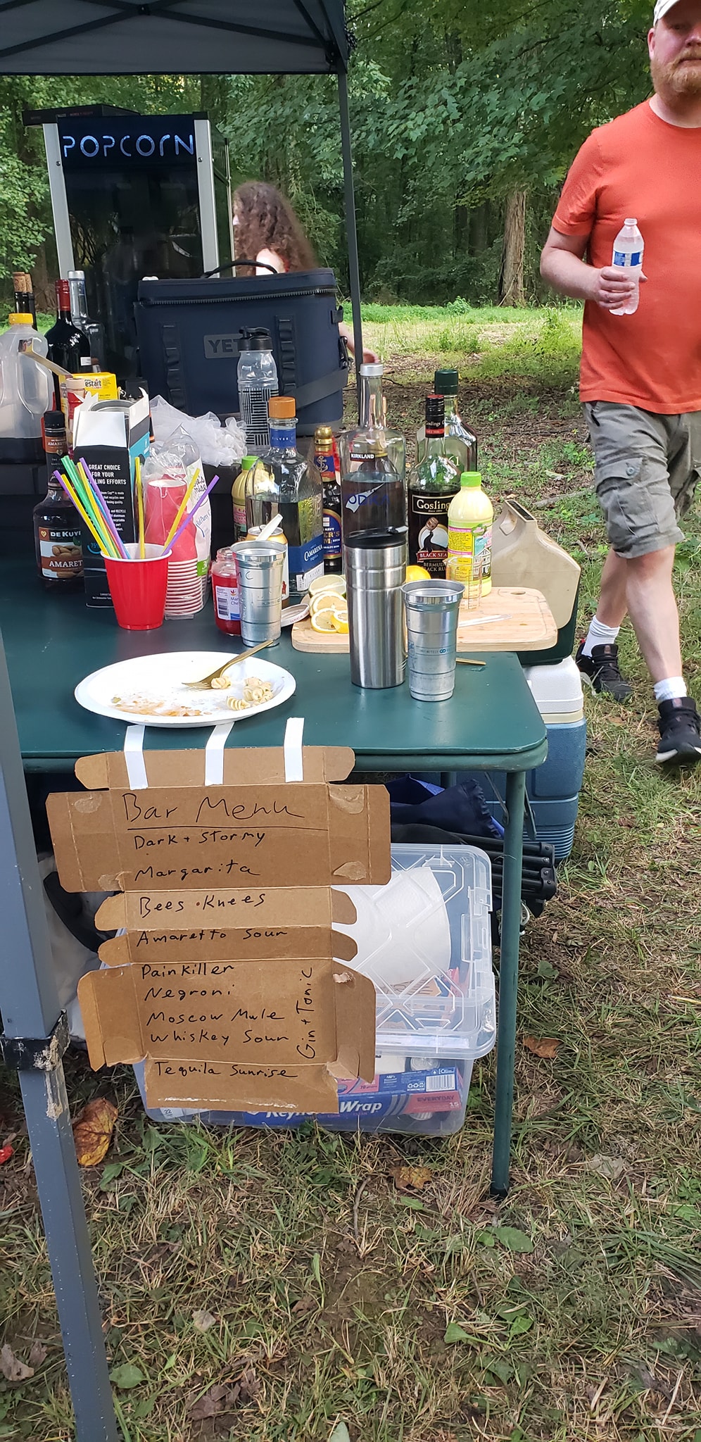 Close-up of the handwritten bar menu with liquor bottles and the popcorn machine — Campout 2024