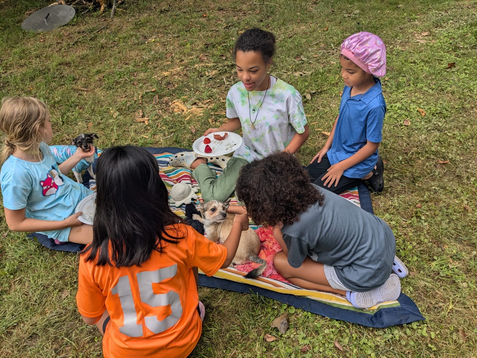 Kids sitting in a circle on a blanket passing around a small dog — Campout 2024