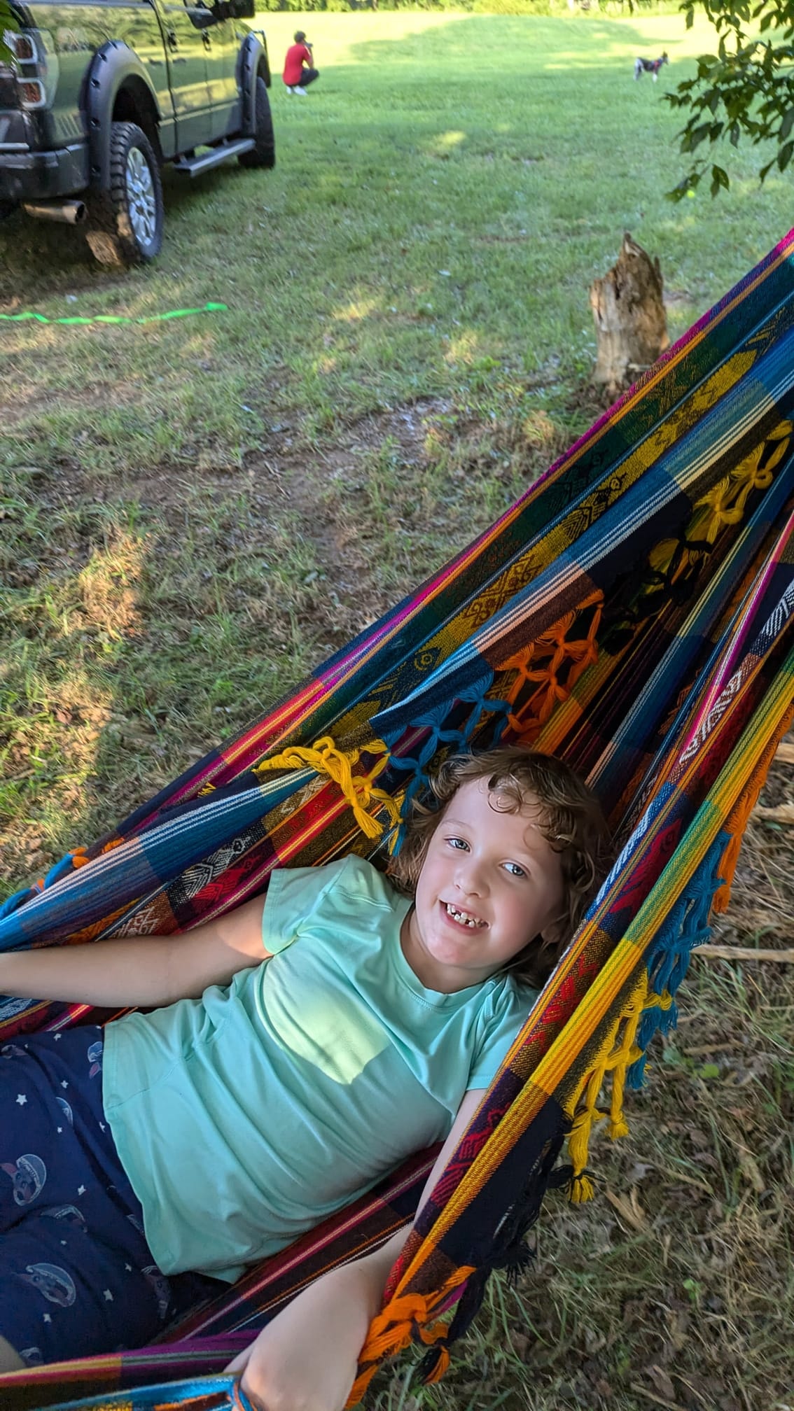 A kid relaxing in a bright colorful hammock strung between the trees — Campout 2024