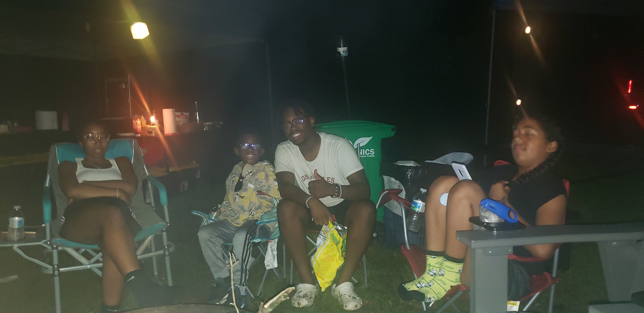 Family in camp chairs late at night, little one sporting 3D glasses — Campout 2024