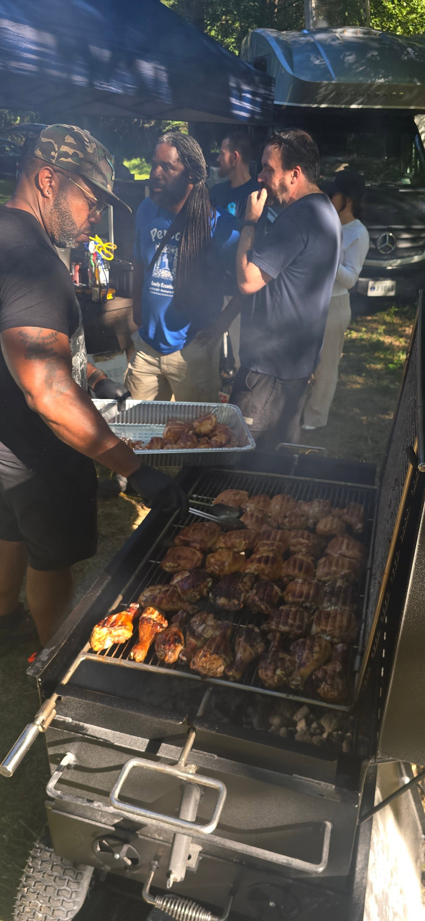 Working the smoker together as smoke drifts up through the trees — Campout 2025