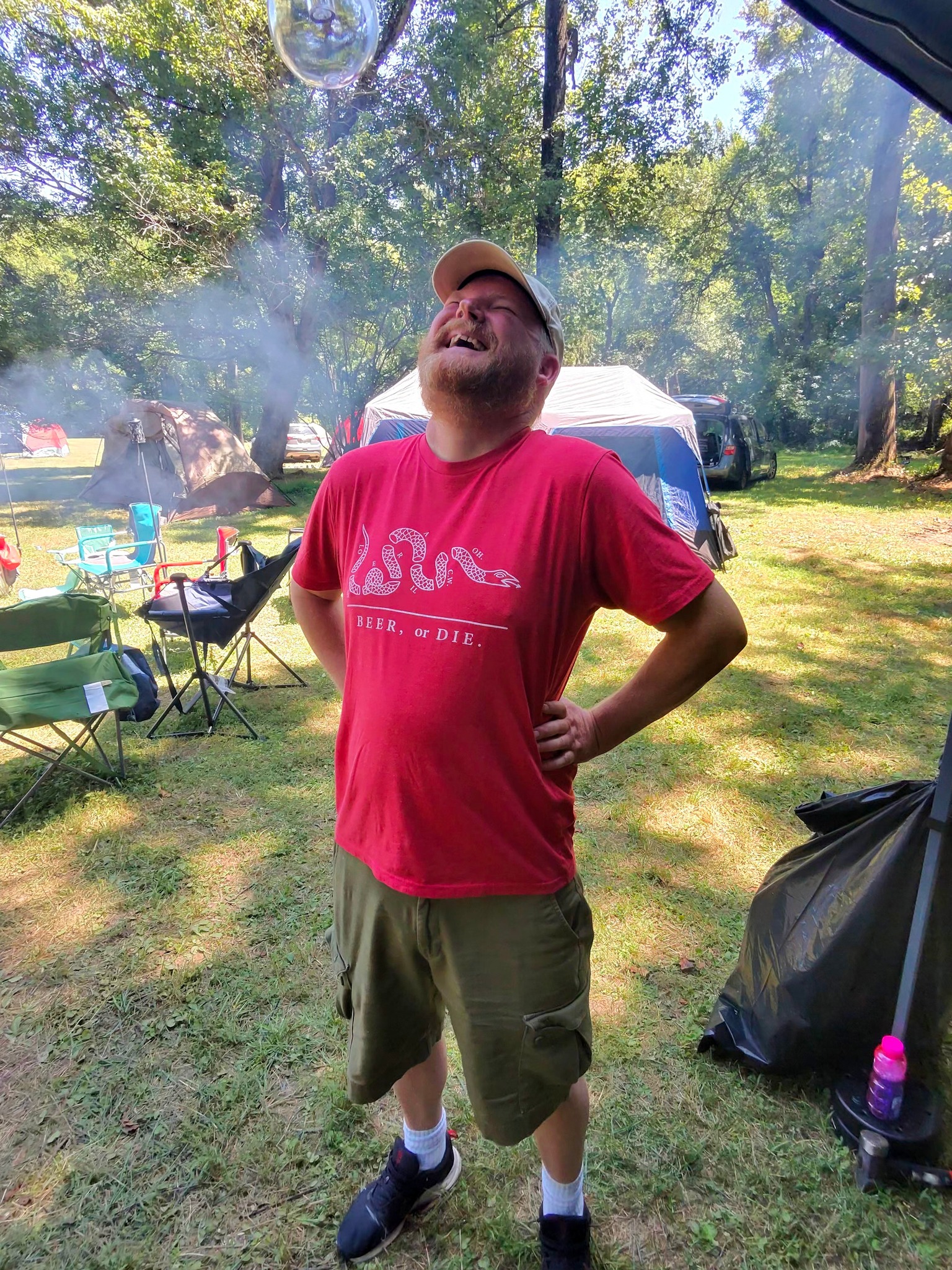 Laughing in a cloud of campfire smoke surrounded by tents — Campout 2025