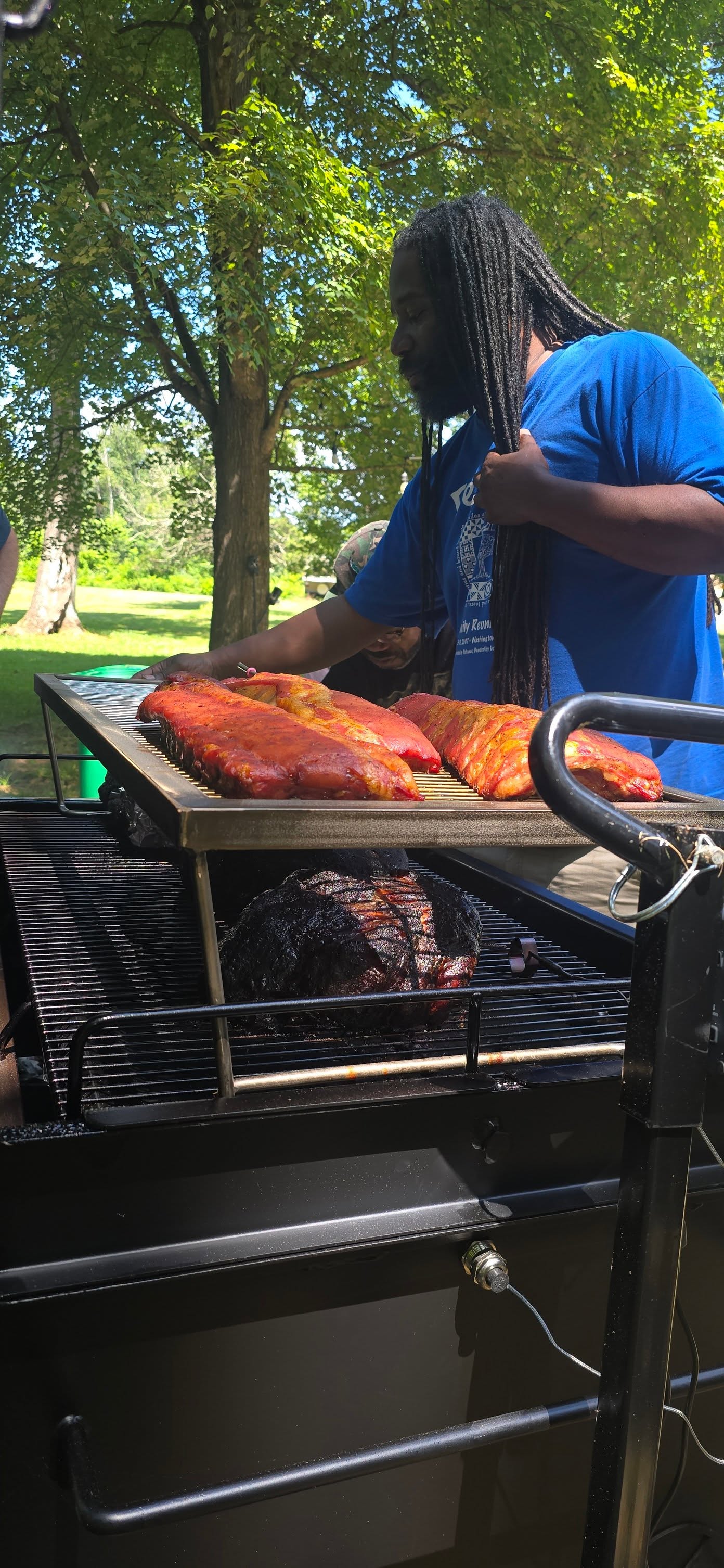 Reaching across the smoker to tend ribs and brisket — Campout 2025