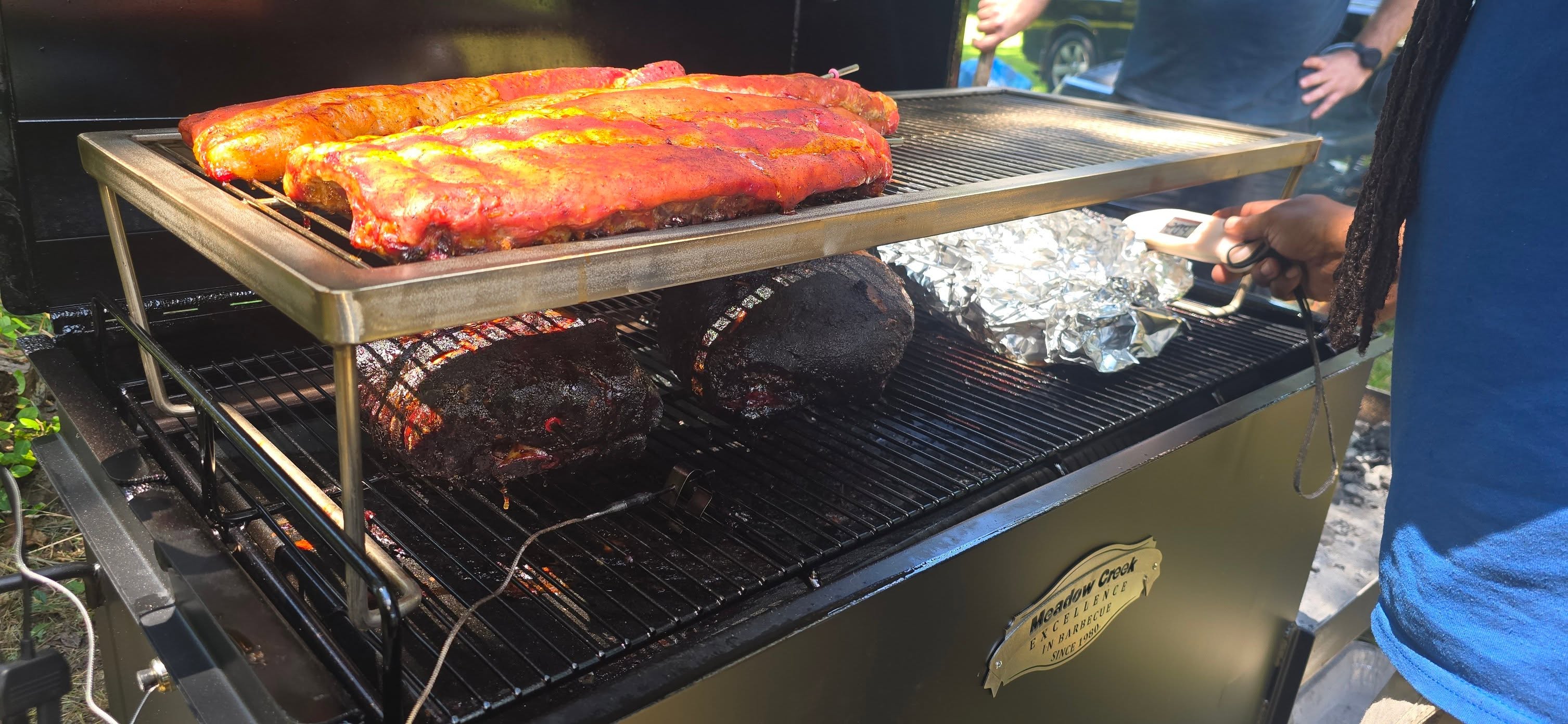 Sauced ribs and brisket on the smoker rack, smoke curling up — Campout 2025