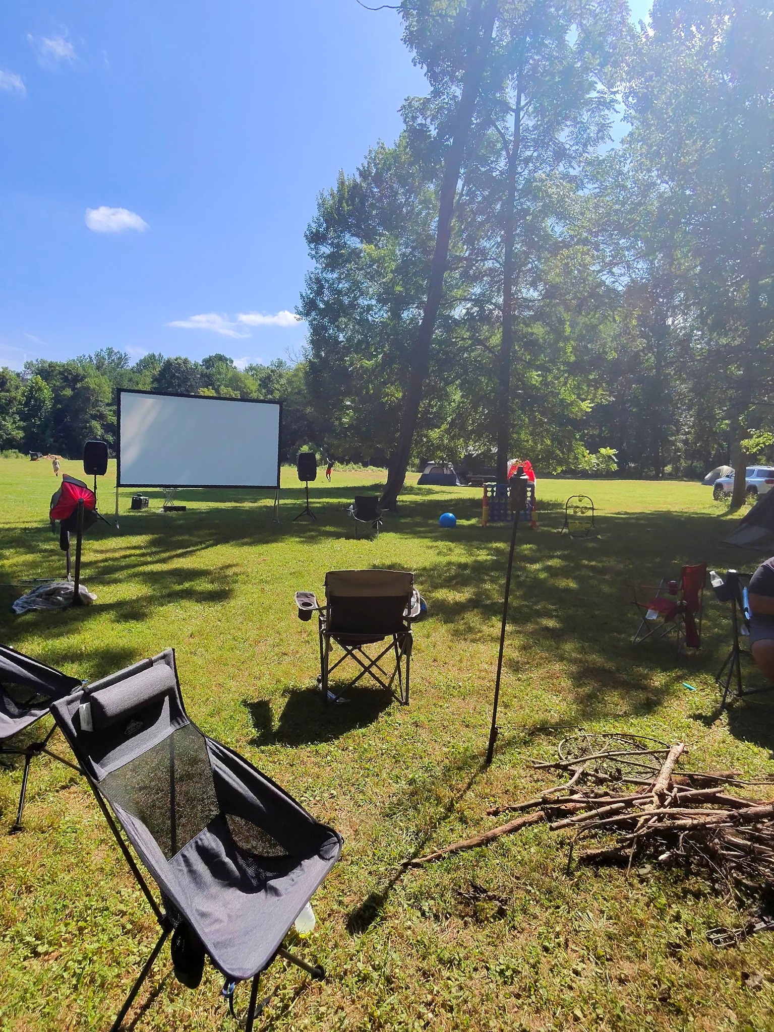 Outdoor movie screen on the open lawn with firewood stacked nearby — Campout 2025