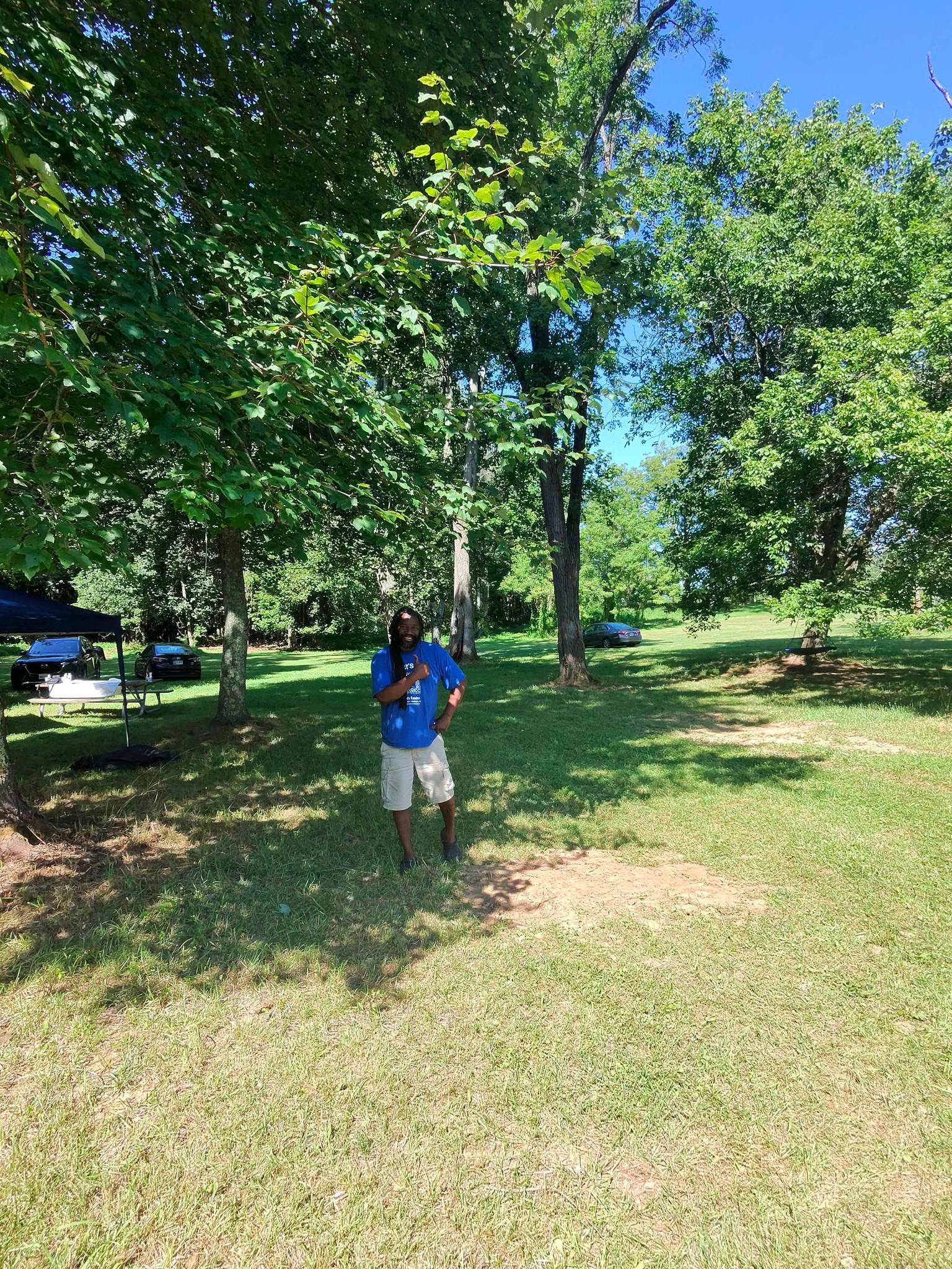 Standing alone on the open lawn beneath tall shade trees — Campout 2025