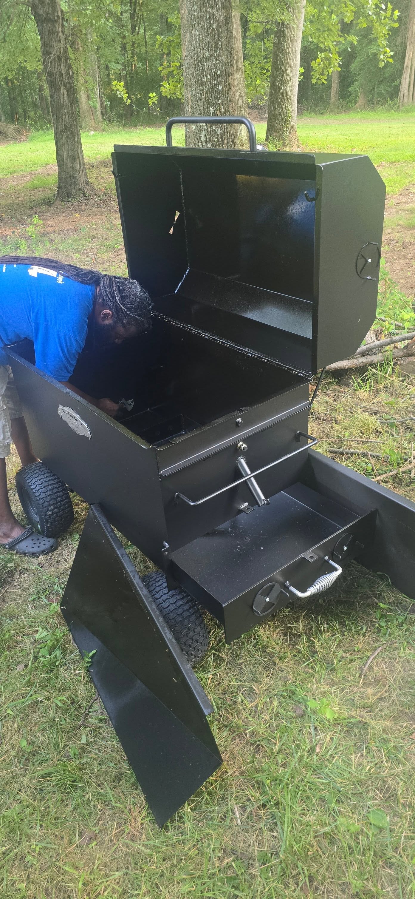 Leaning into the open smoker to check on the meat inside — Campout 2025