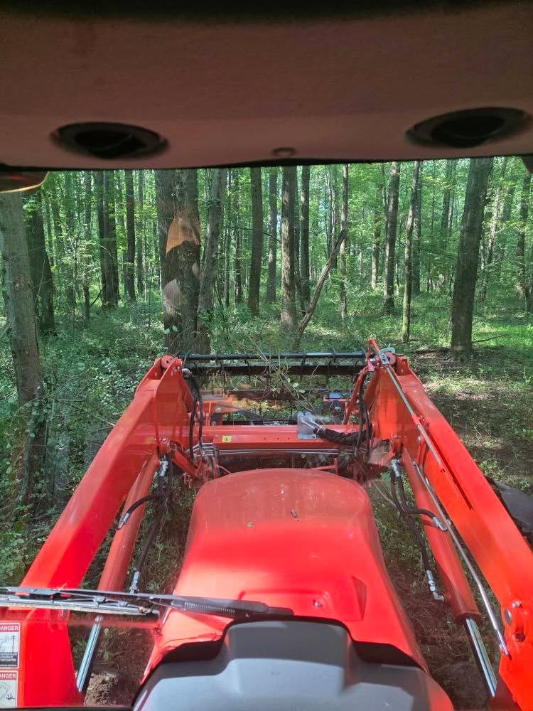 View from inside a tractor cab looking out over the wooded property — Campout 2025