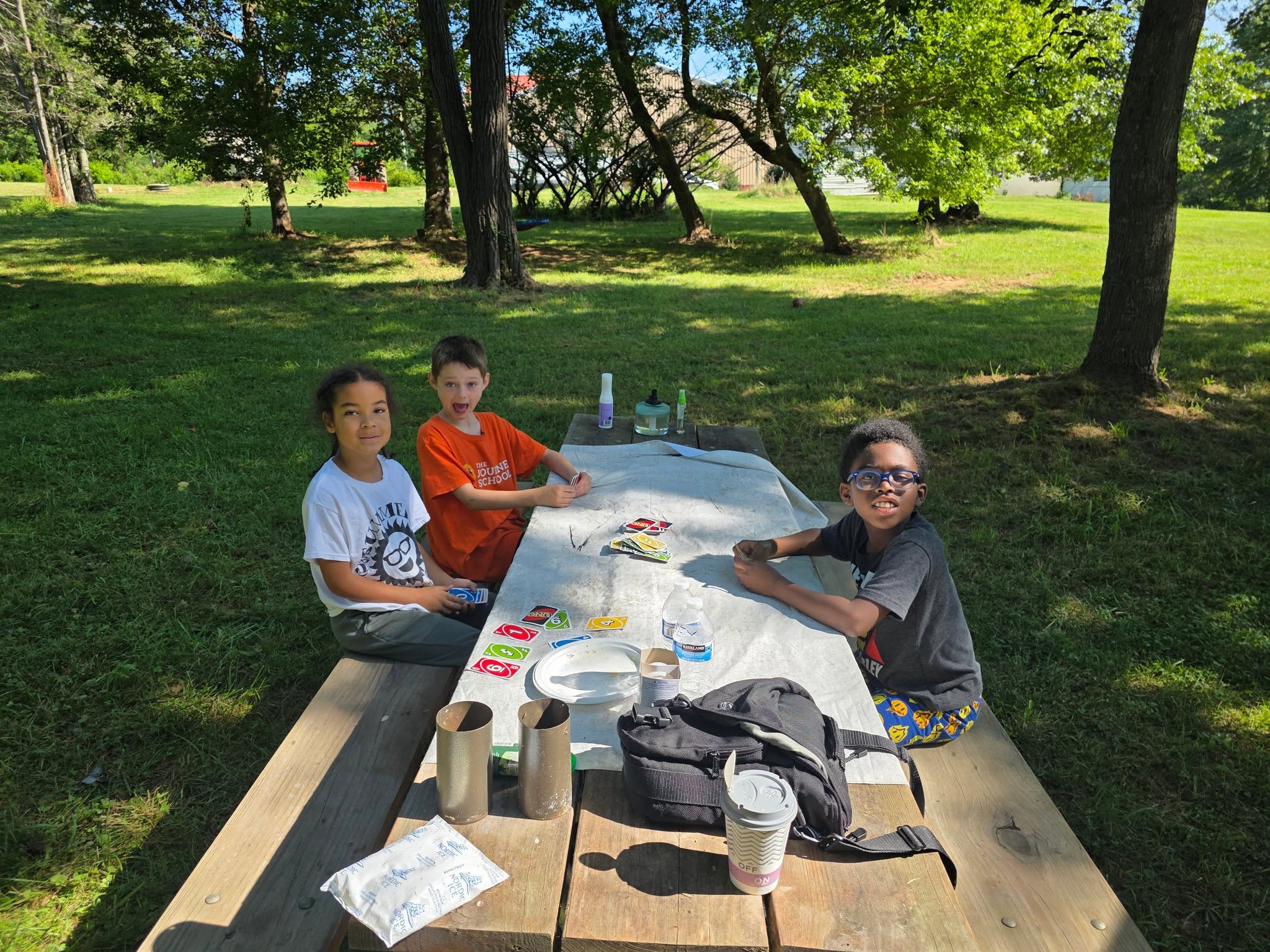 Kids playing cards at a picnic table in the shade — Campout 2025