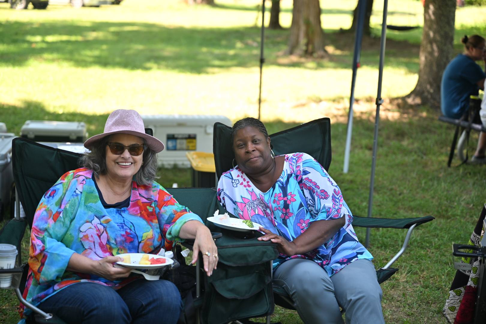 Guests with plates of food relaxing in camp chairs in the afternoon sun — Campout 2025