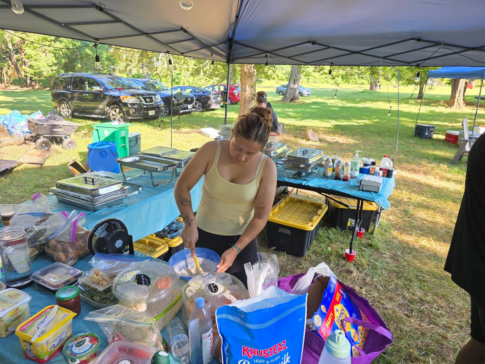 Prepping food under the catering canopy with pans and supplies spread out — Campout 2025