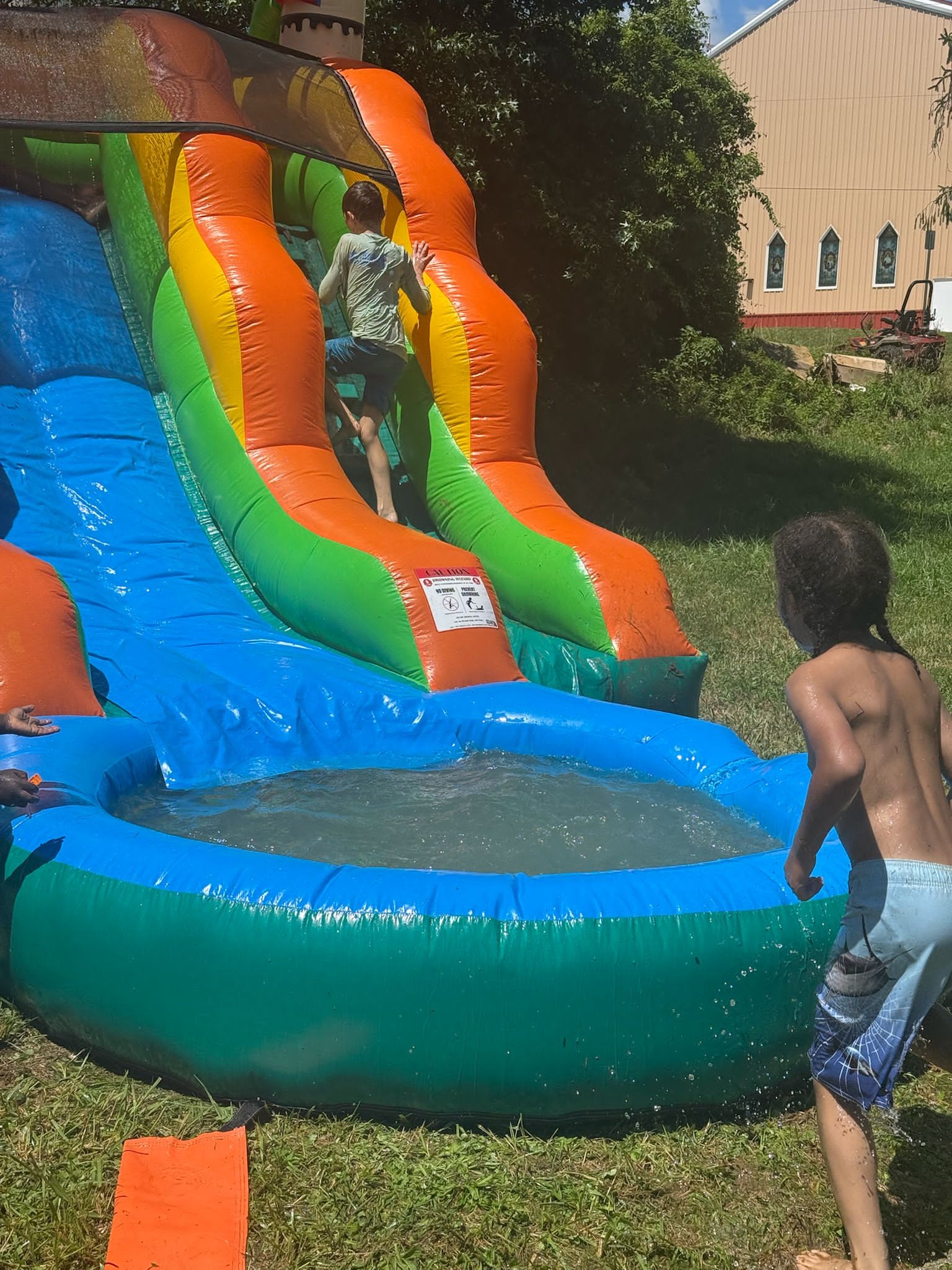 Kids racing toward the inflatable water slide on a bright summer day — Campout 2025