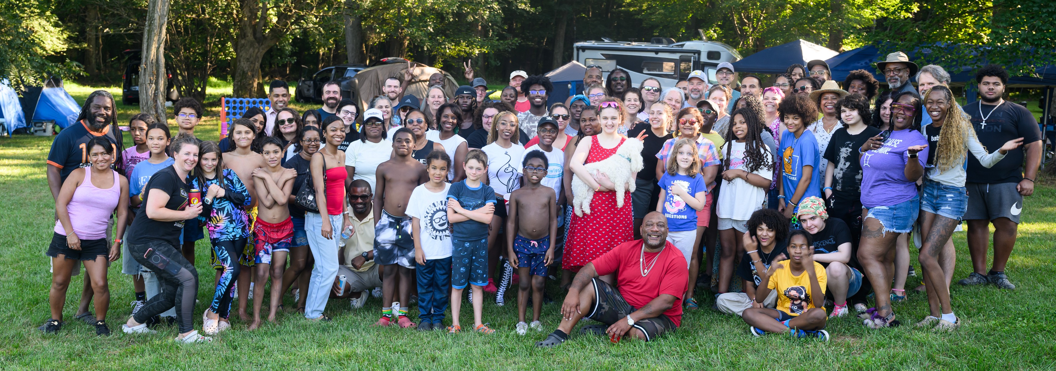 Group photo on the lawn with tents and tall trees behind — Campout 2025